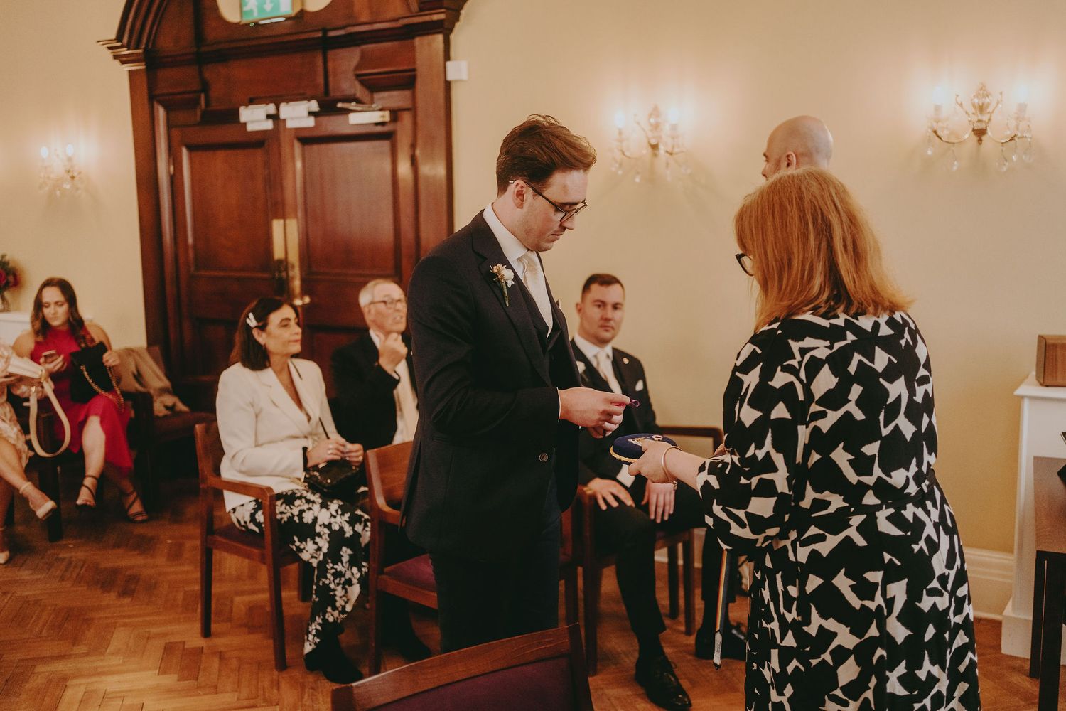 Wedding ceremony taking place in elegant room with hardwood floors and cream walls.