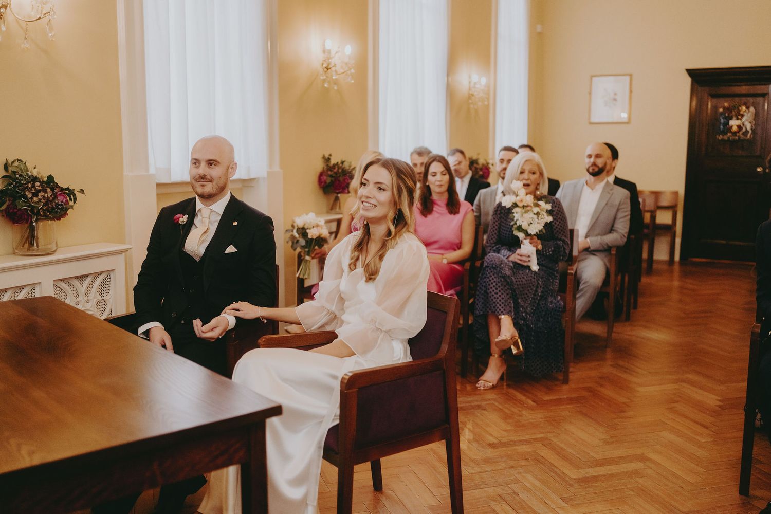 Guests seated in elegant room with herringbone floors and crystal chandelier.