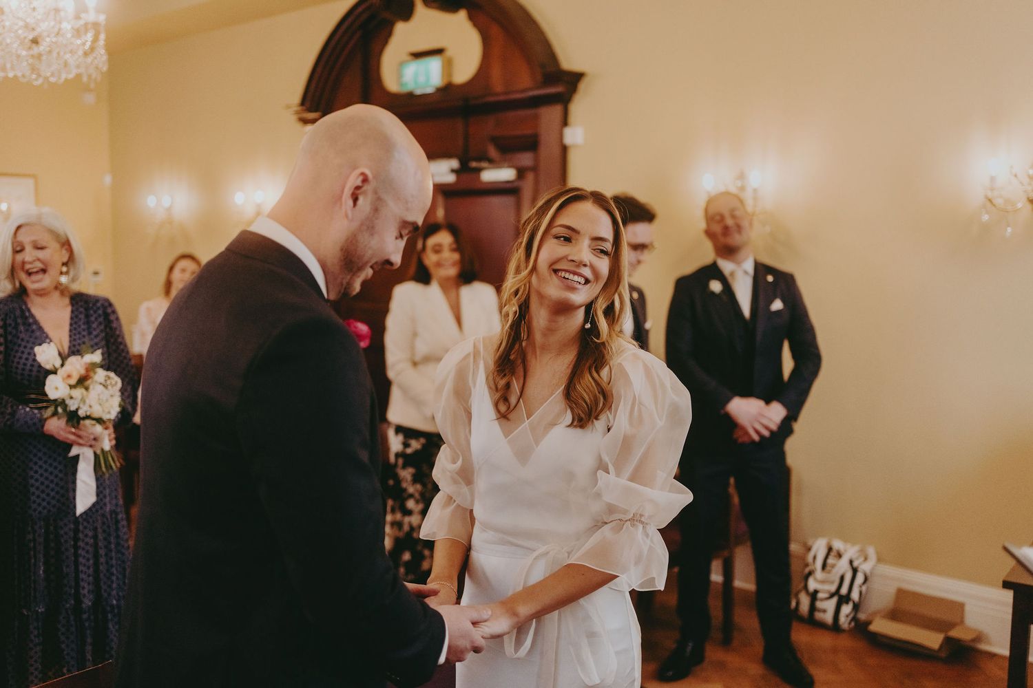 Wedding ceremony moment in elegant room with antique clock and wall sconces.