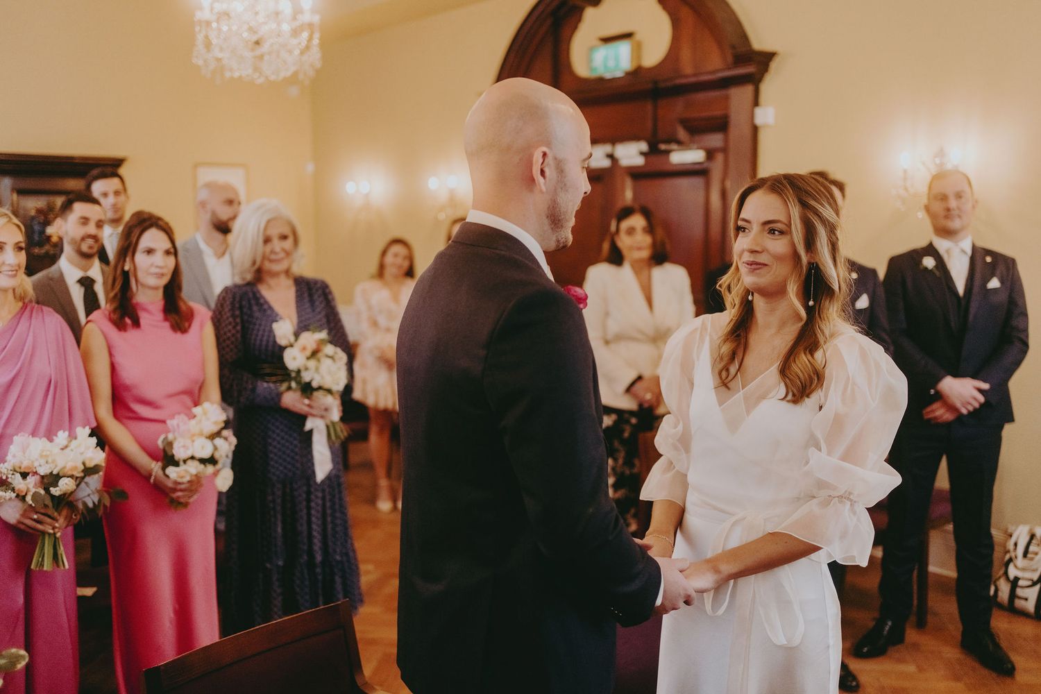 Wedding ceremony in progress with pink-clad bridesmaids and guests watching.