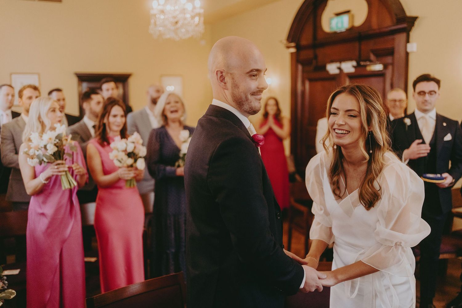 Joyful wedding ceremony moment with guests in pink dresses looking on.