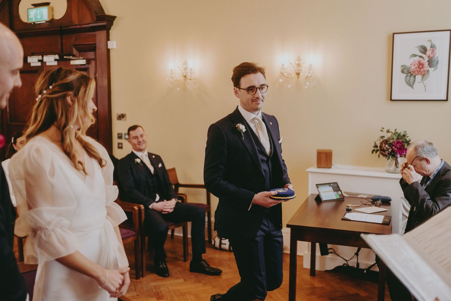 An intimate wedding ceremony takes place in an elegant room with wooden details and wall sconces.