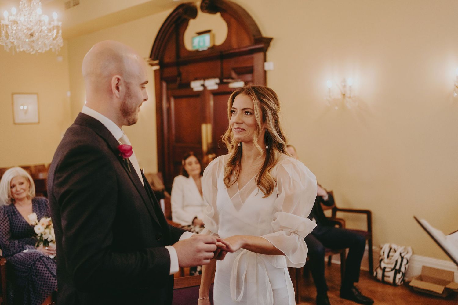A couple shares a joyful moment during their wedding ceremony in a warmly lit room with classic decor.