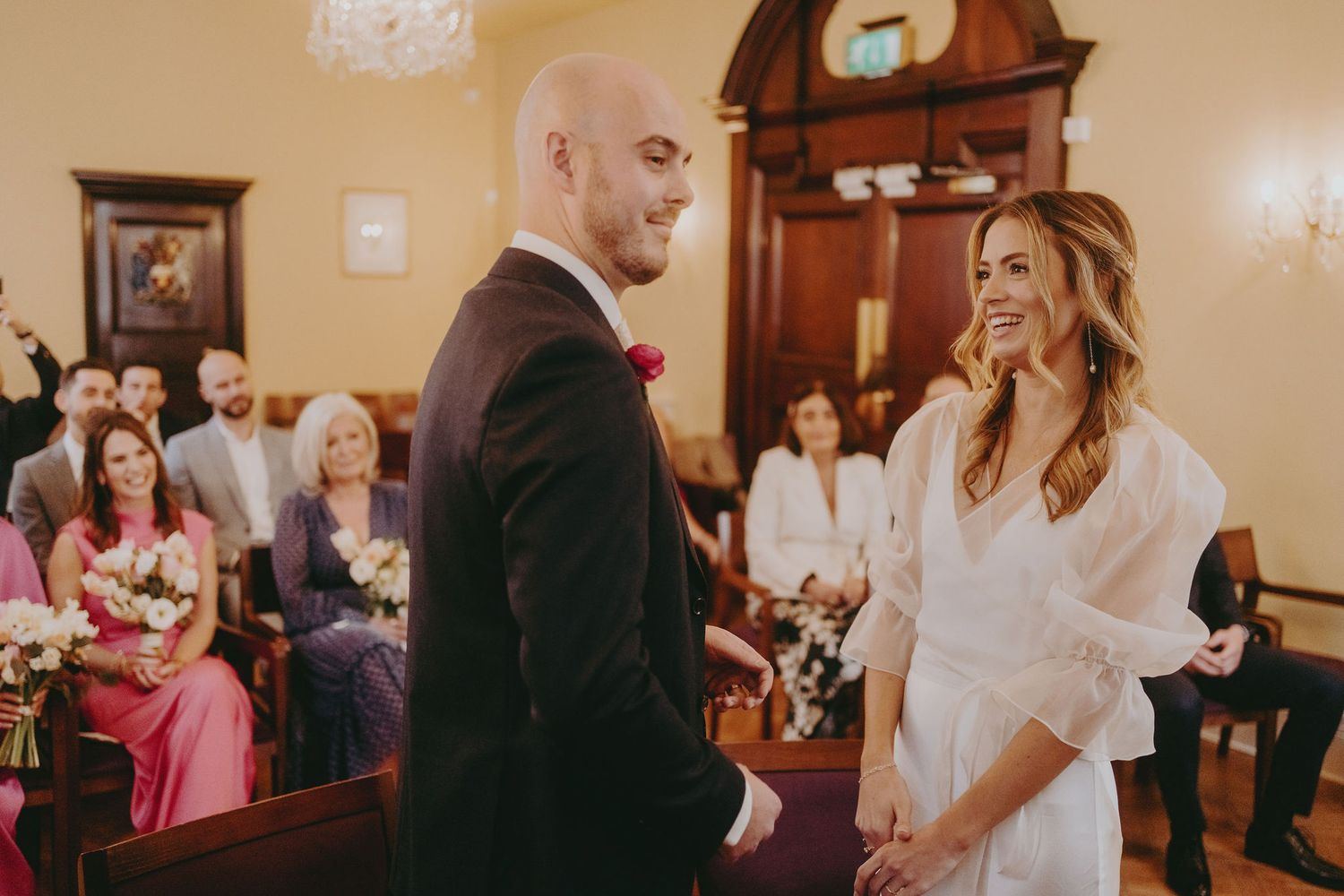 A candid moment during a wedding ceremony shows laughter and joy in an elegant indoor setting.
