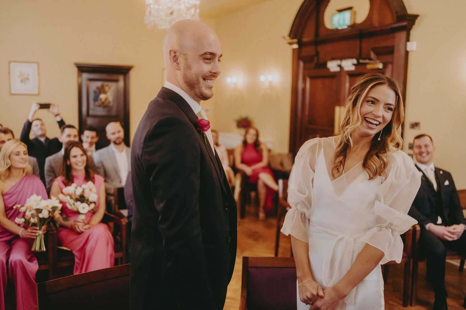 A heartfelt moment shared during an indoor wedding ceremony with pink-clad bridesmaids in attendance.