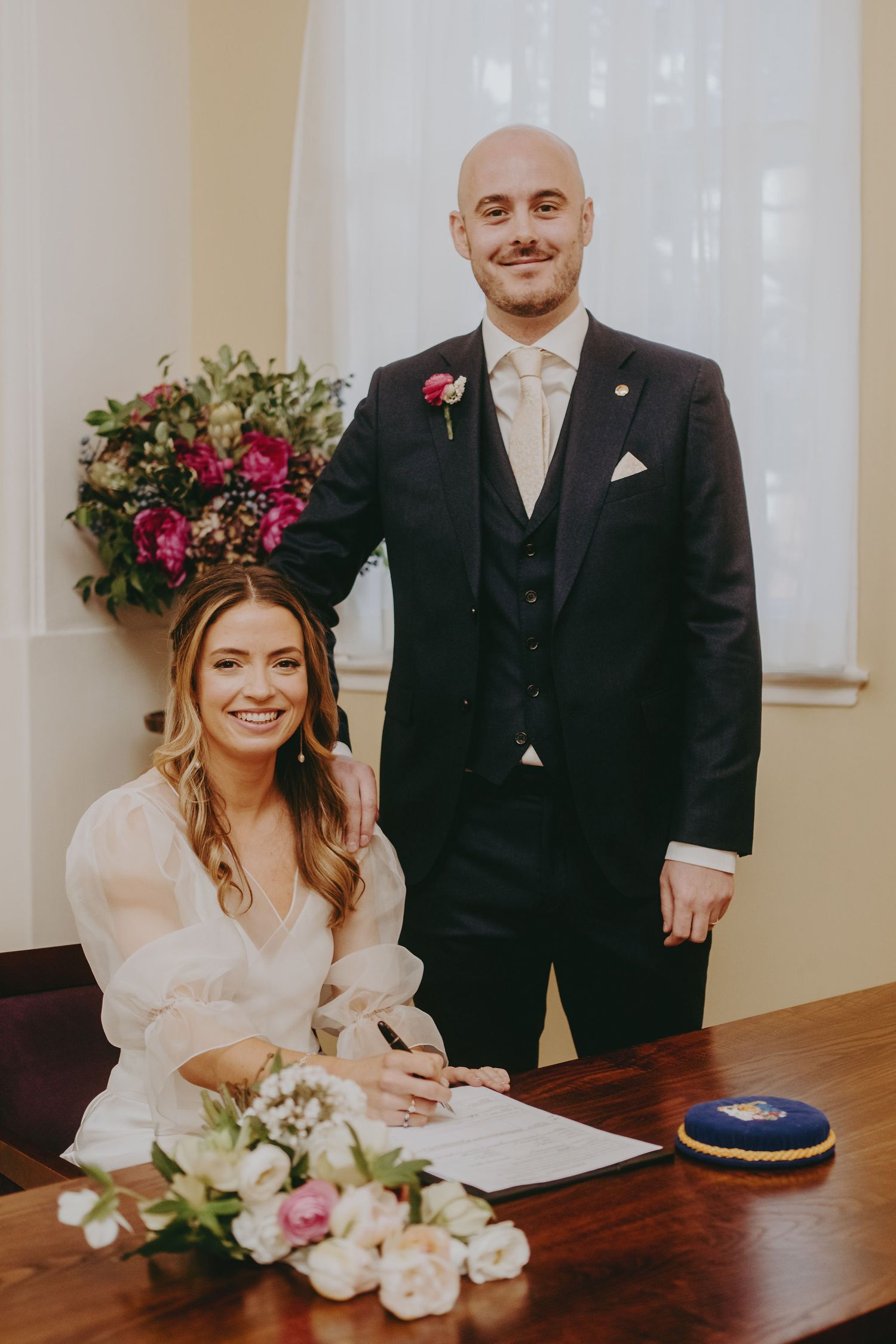 Wedding couple poses at signing table with floral decorations during their civil ceremony.