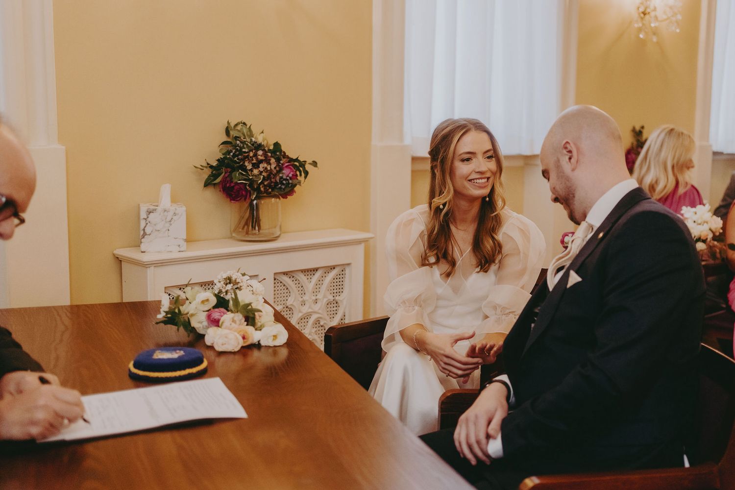 Wedding couple engages in conversation during civil ceremony registration with guests looking on.