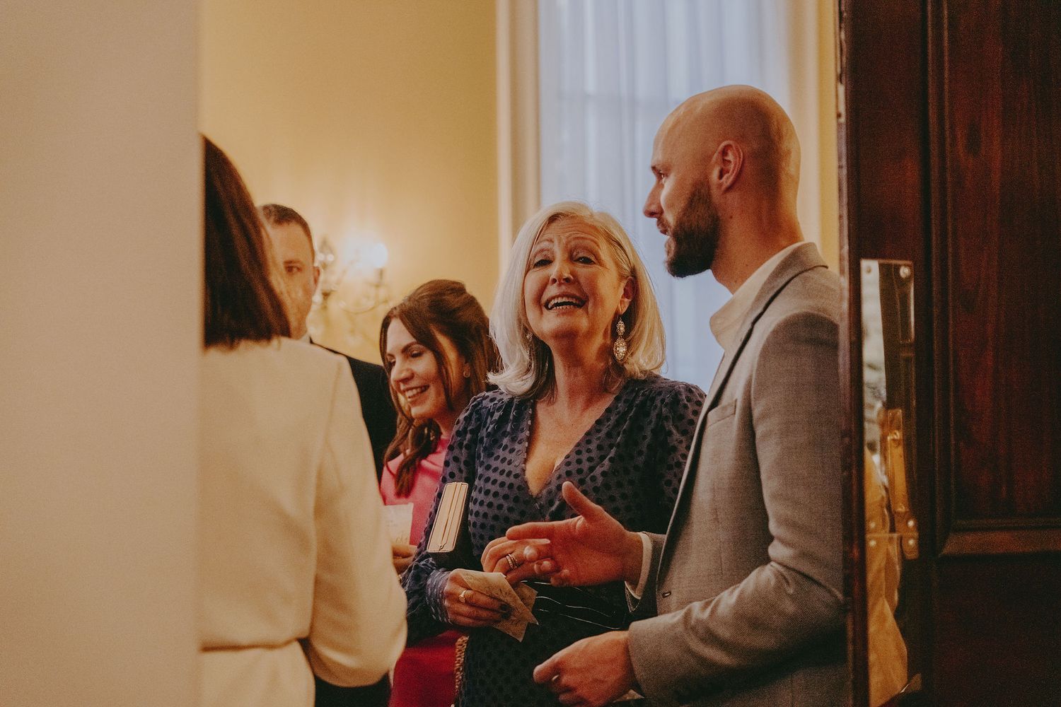 Wedding guests share joyful moments and conversation in a brightly lit hallway.