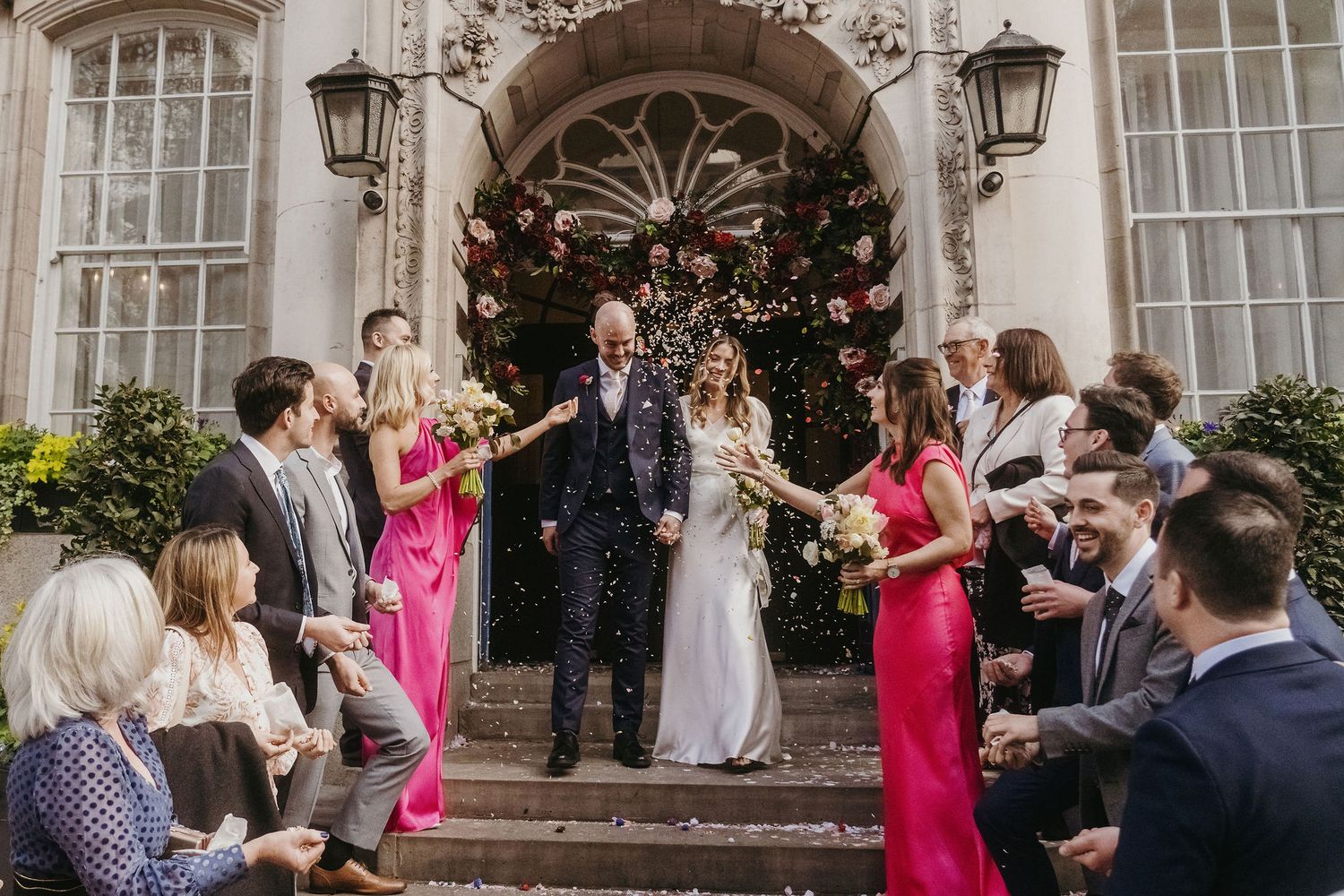 Newlyweds exit historic building as guests throw confetti on ornate stone steps.