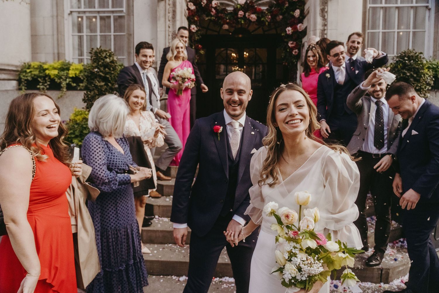Joyful wedding celebration on elegant stone steps with guests in vibrant attire.