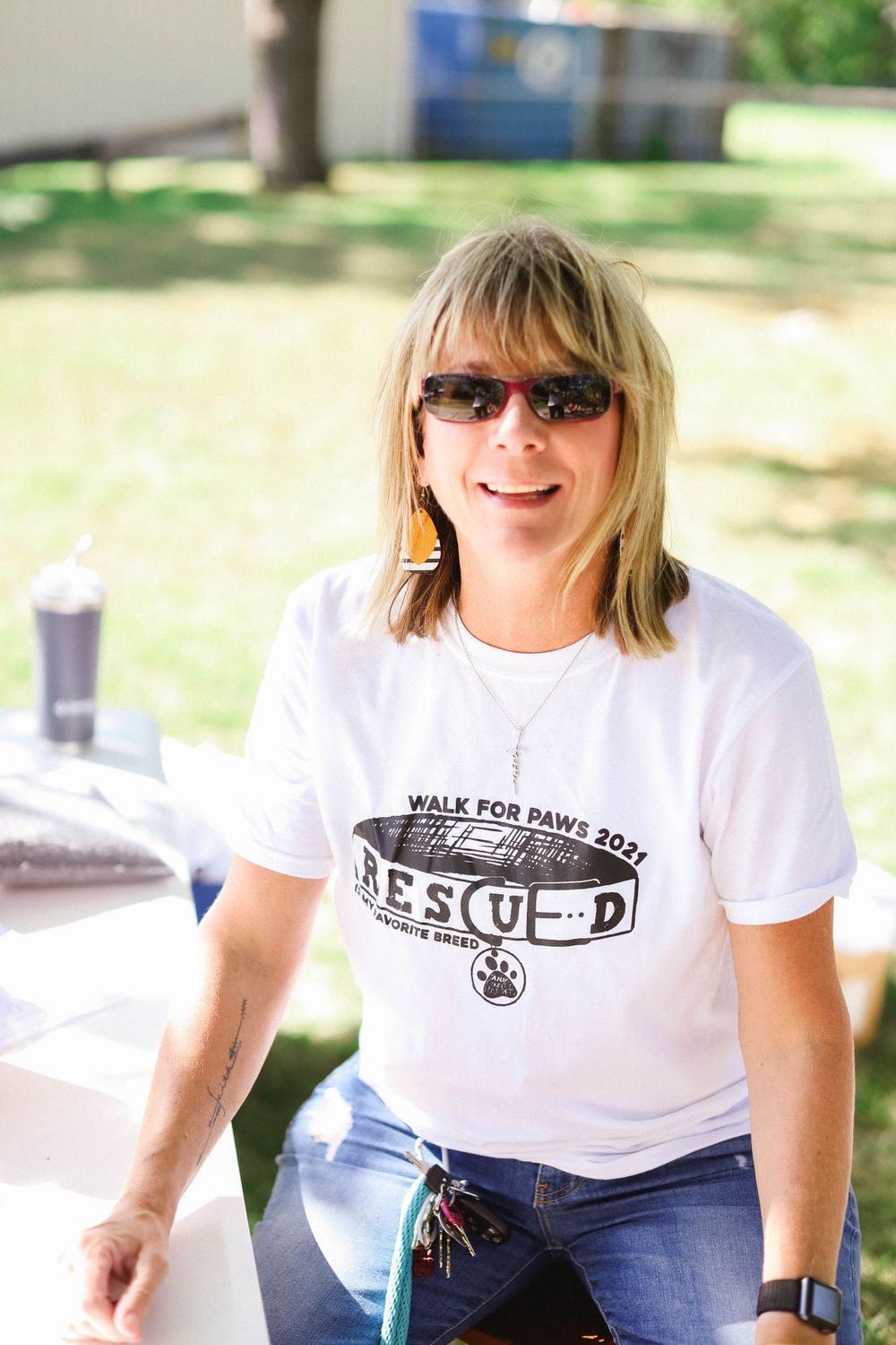 Person wearing Walk for Paws t-shirt and sunglasses sitting outdoors.