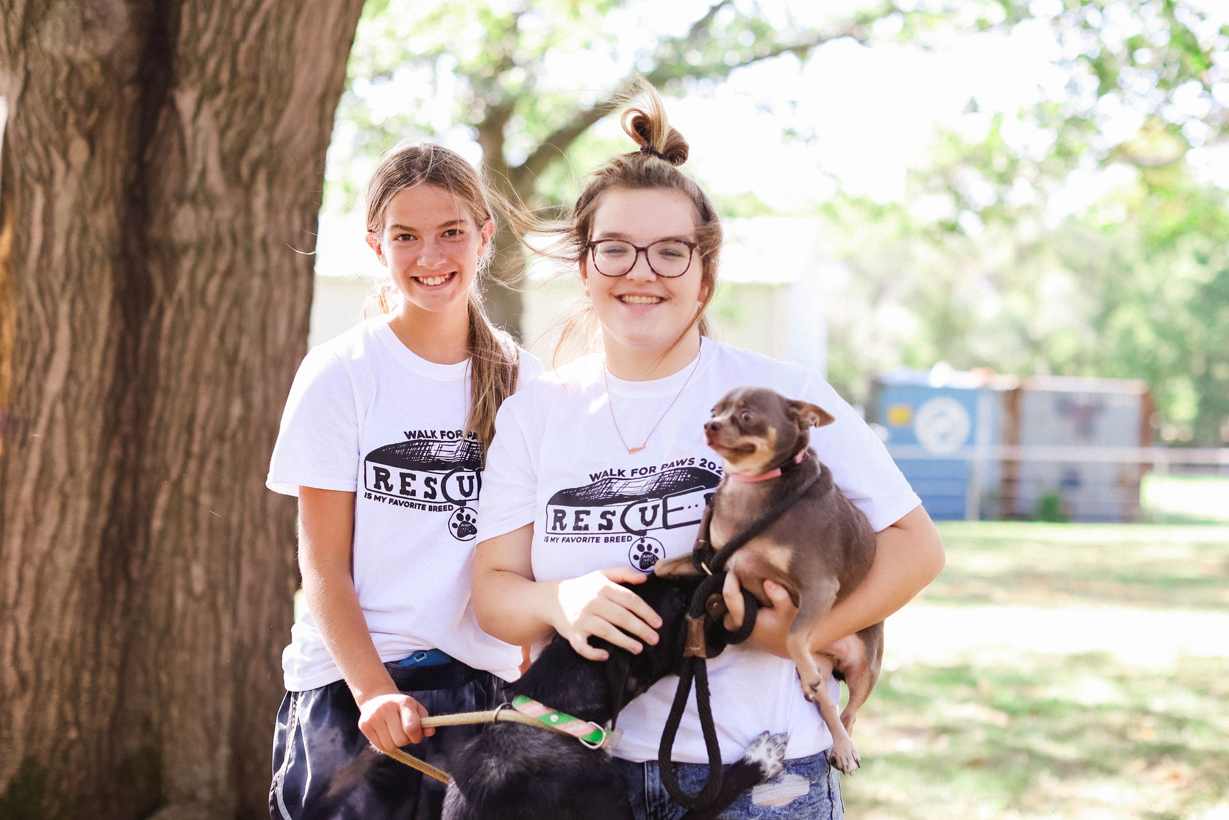 People wearing matching t-shirts pose with dogs at an outdoor gathering.