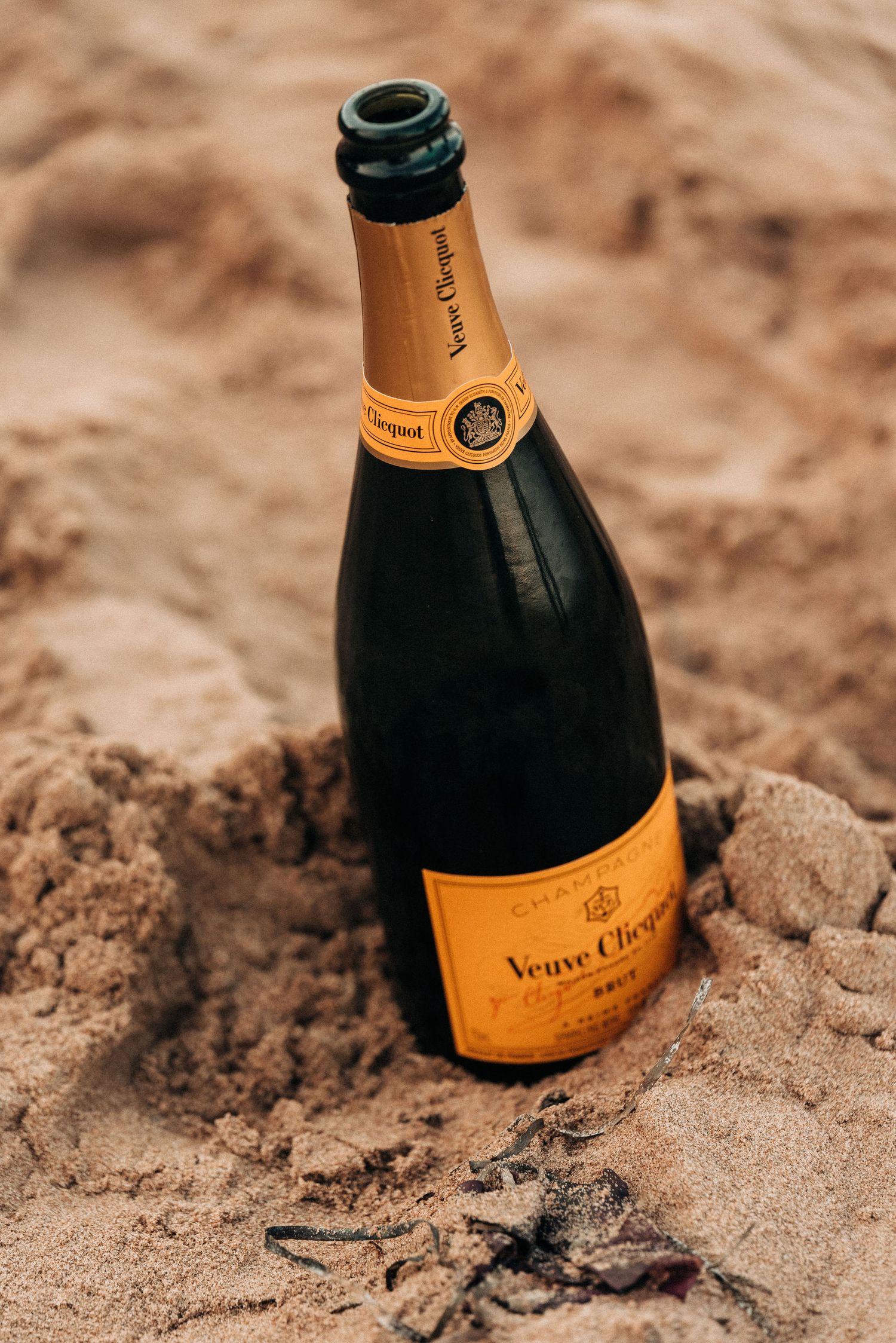 Veuve Clicquot champagne bottle nestled in beach sand.