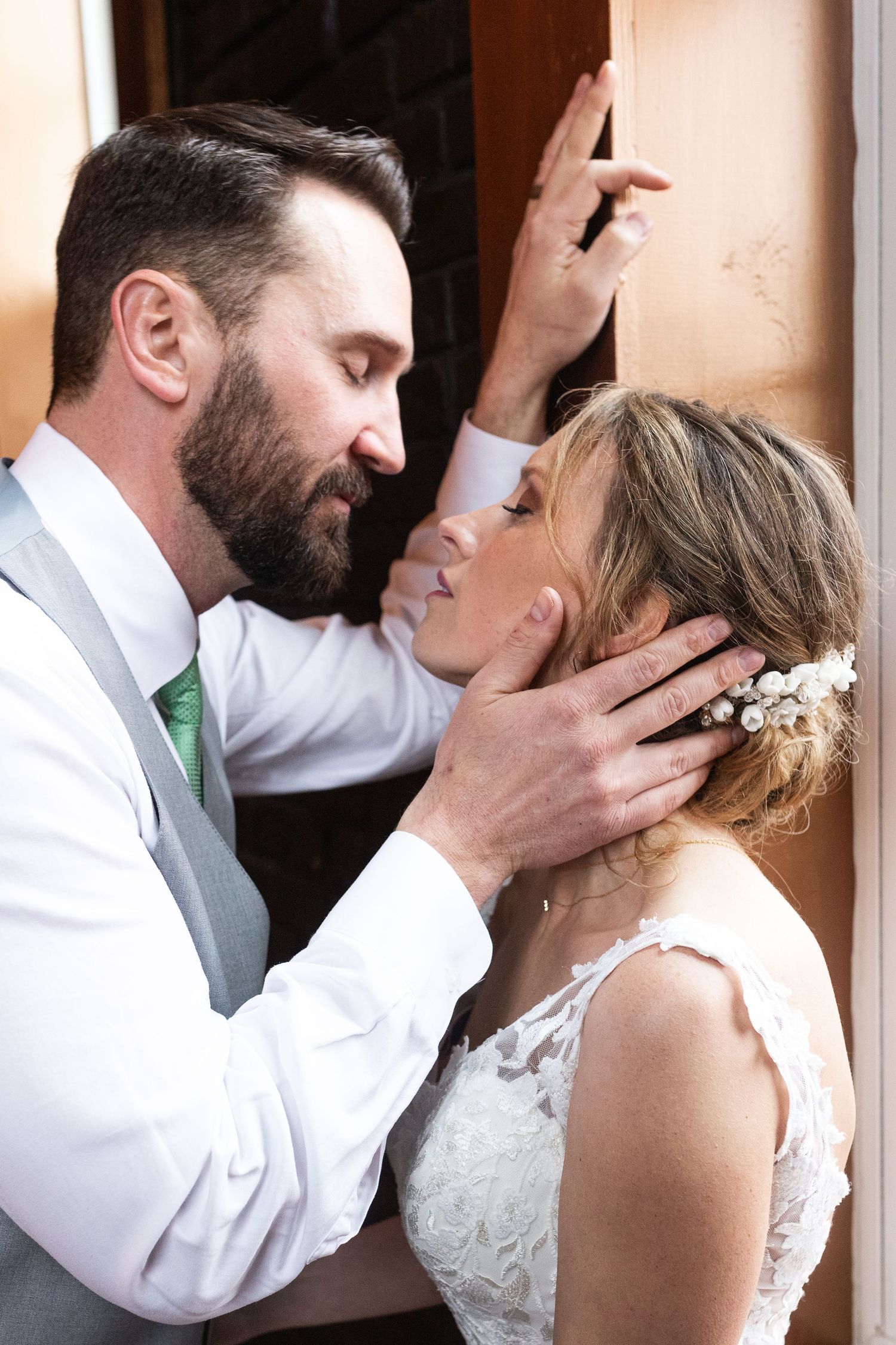 Intimate moment between newlyweds against rustic wall backdrop.