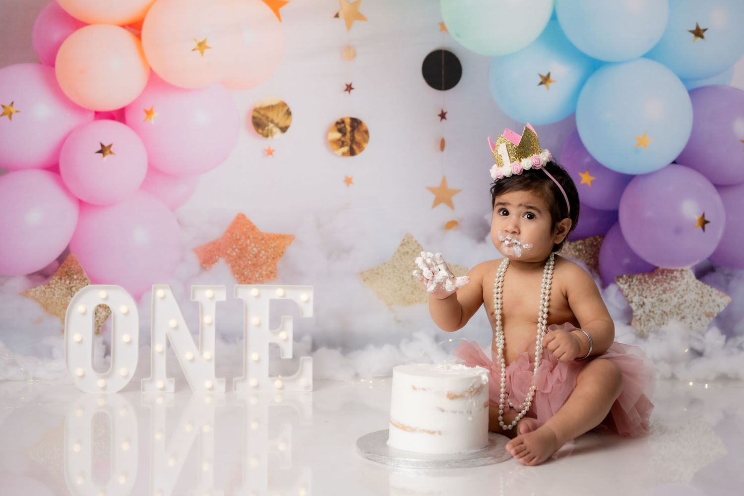 First birthday cake smash setup with pastel balloons and sparkly decorations.