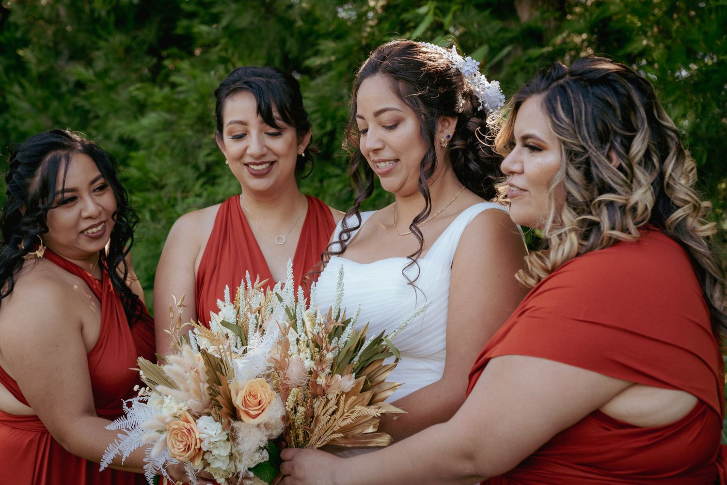 Bride with two bridesmaids smiling, holding boho bouquets. Joyful pre-ceremony portrait.