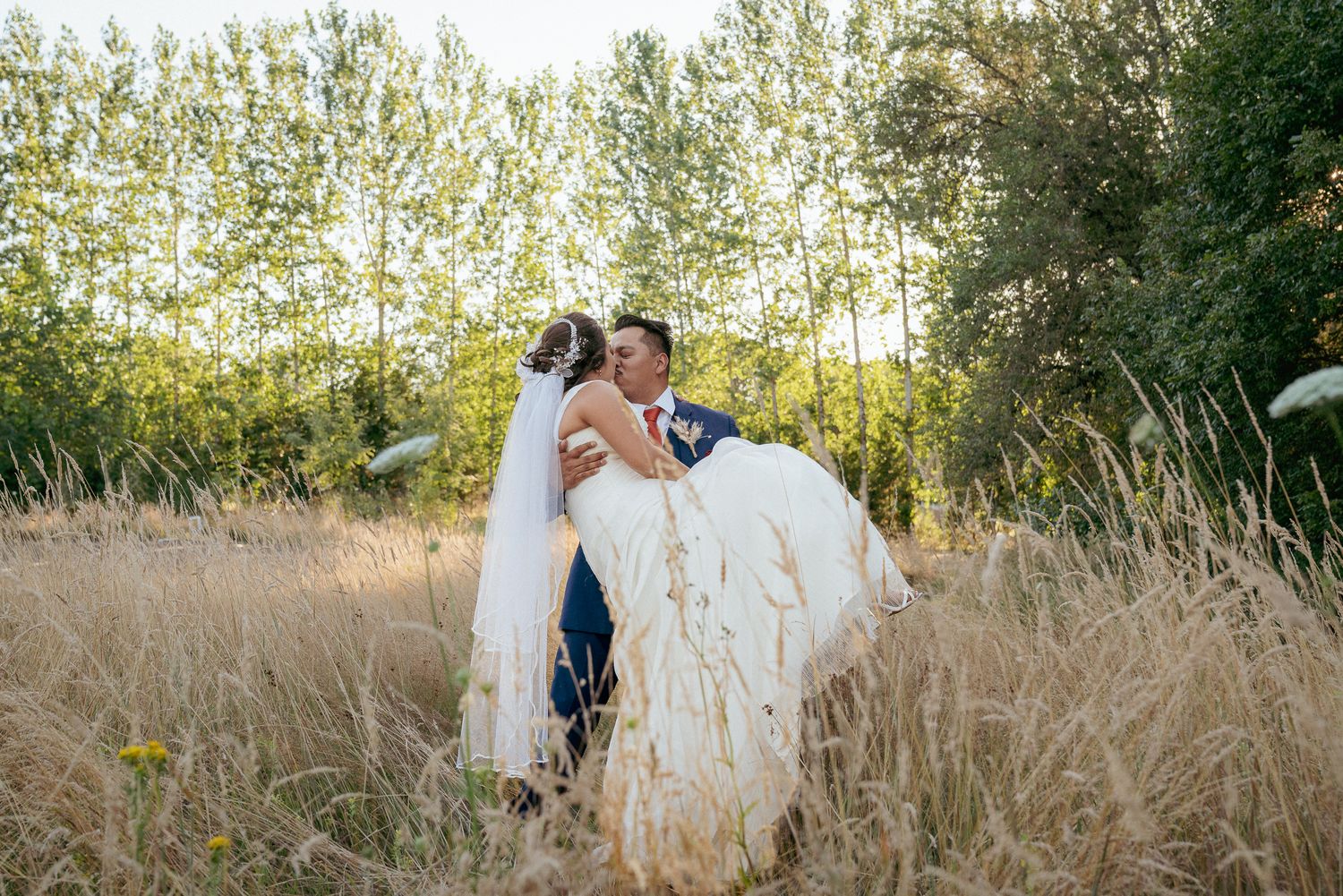 Groom caring the bride and kissin in golden field at sunset, rustic Oregon wedding romance.
