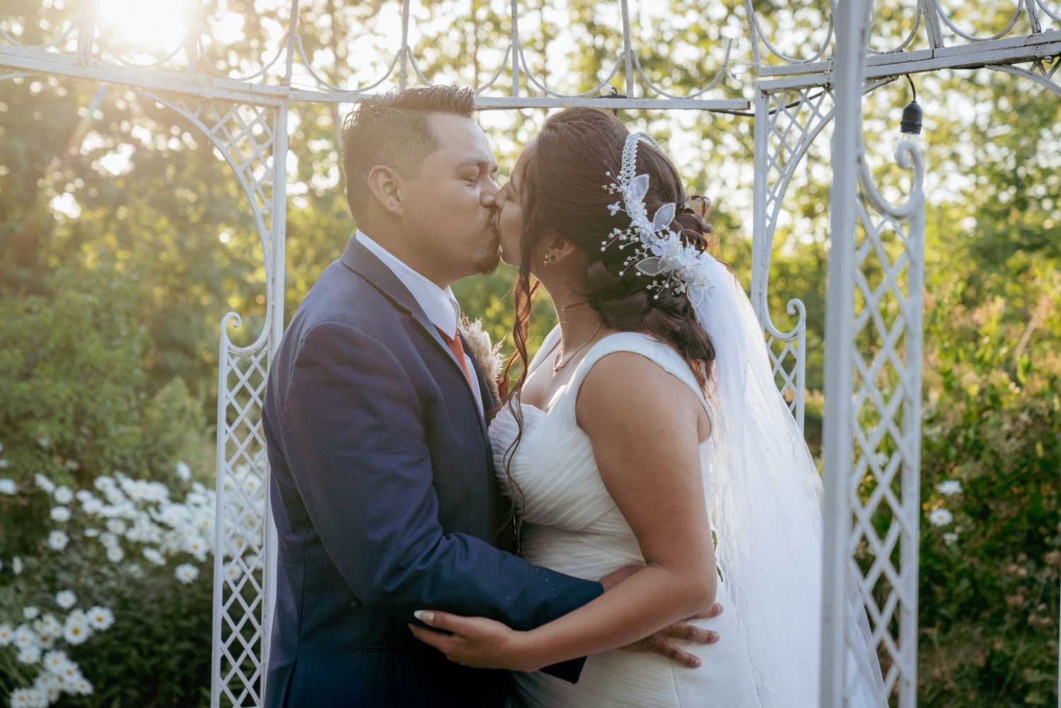 Latinx couple kisses under metal arch, romantic backyard PDX vows.