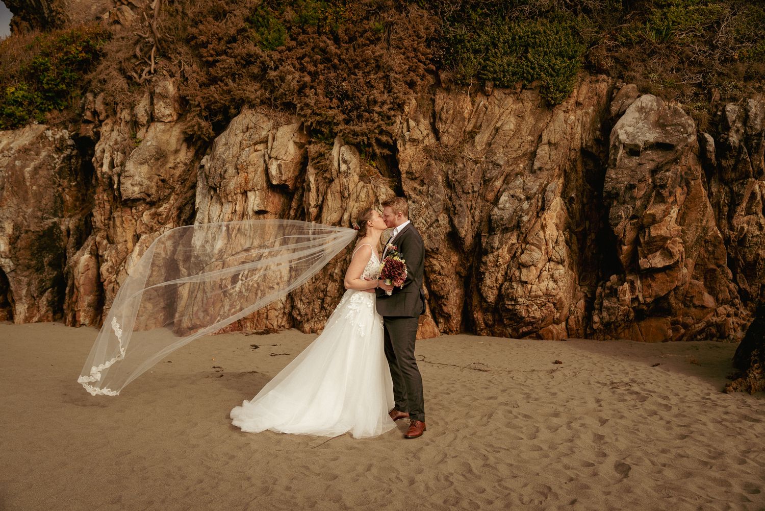 Couple kisses under cliffside arch, golden Oregon Coast elopement.