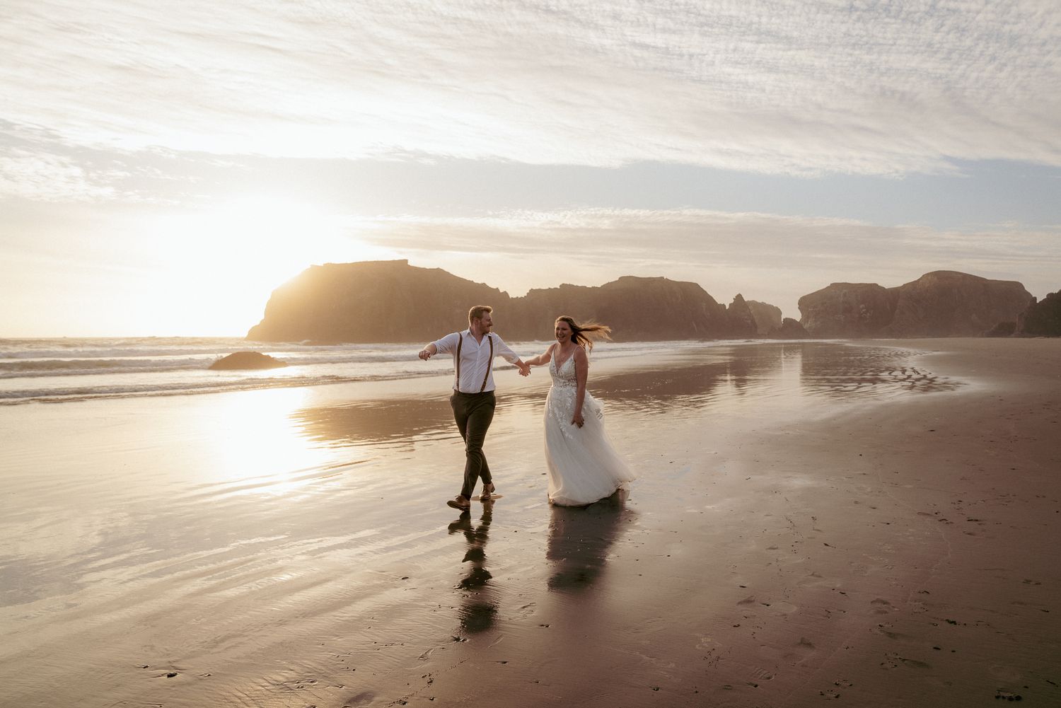 Interracial couple walks hand in hand at Oregon Coast sunrise.