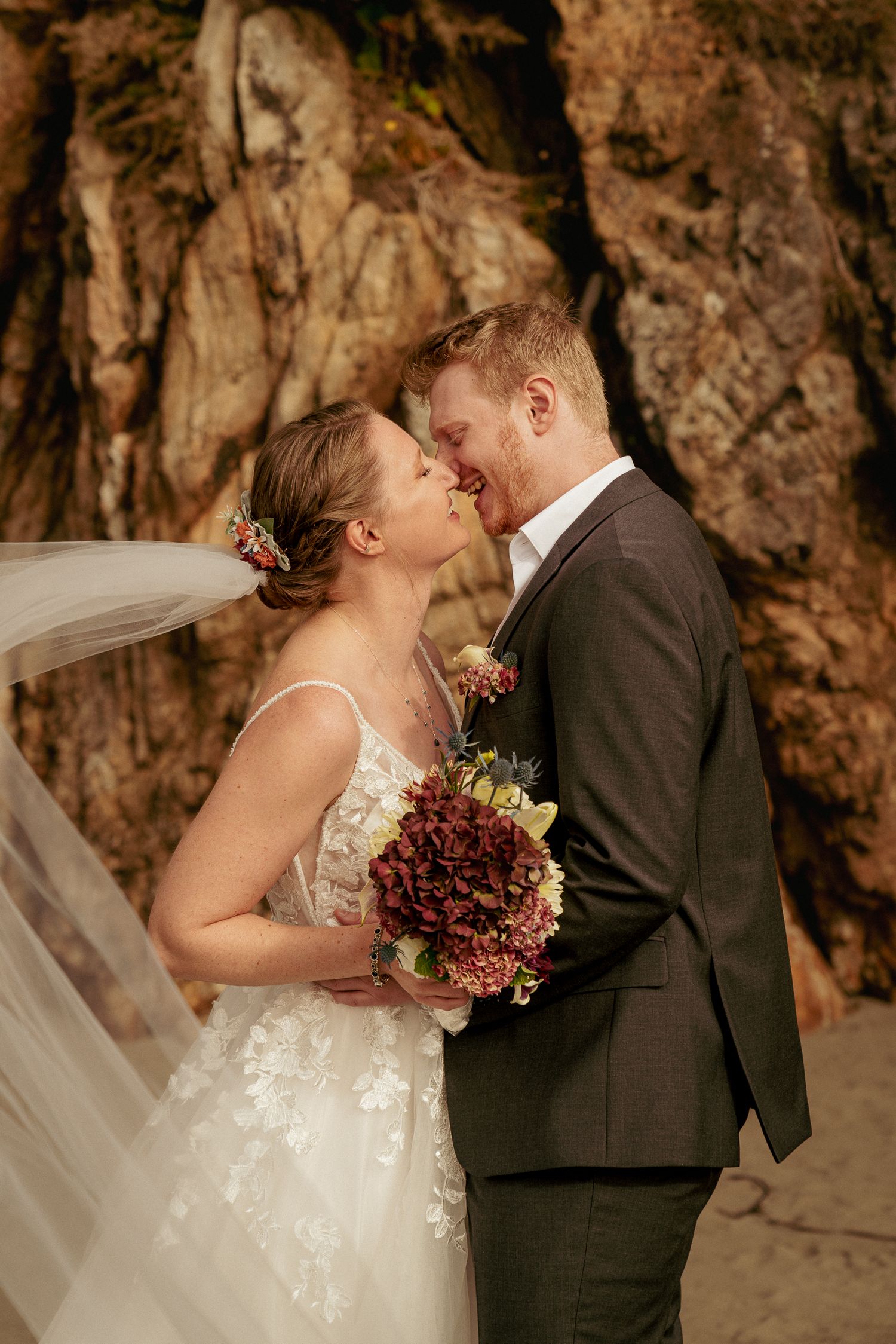 Bride and groom kissing in front of rocky backdrop. South Oregon Coast wedding.