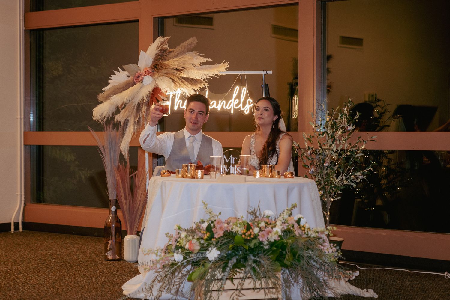 Bride and groom toast behind boho table setup, indoor Oregon reception.