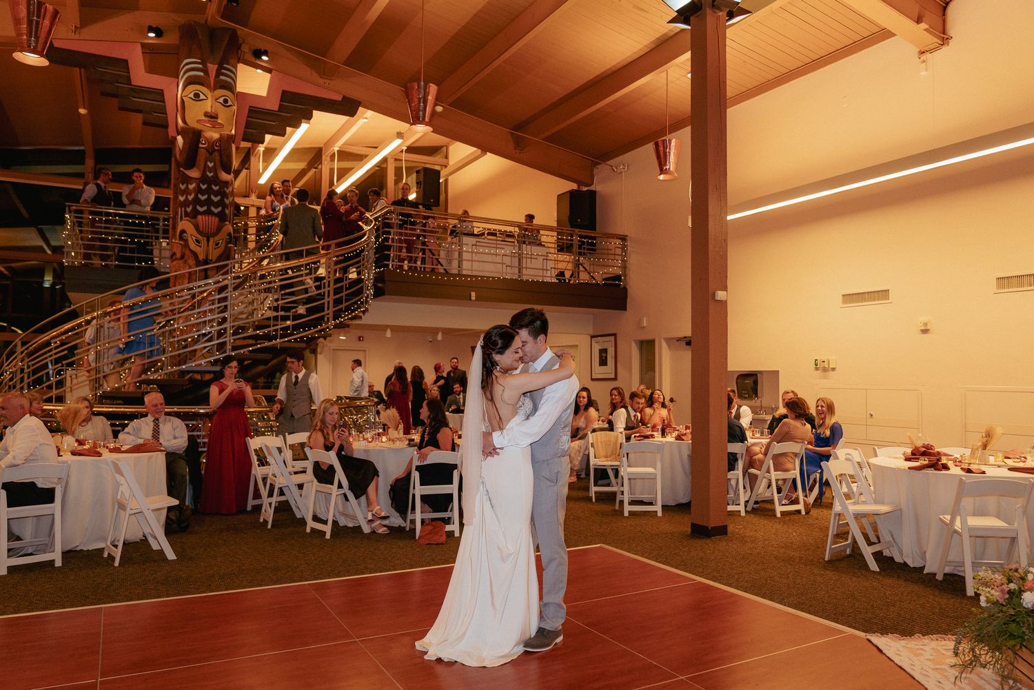 Couple dances in lodge venue with string lights, rustic PNW reception.