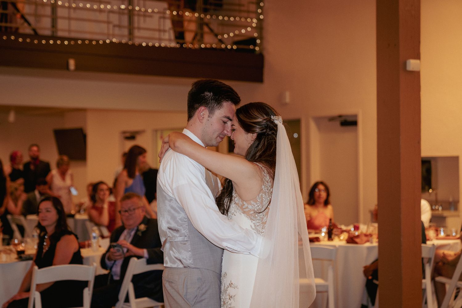 Newlyweds share emotional first dance, indoor PNW reception.
