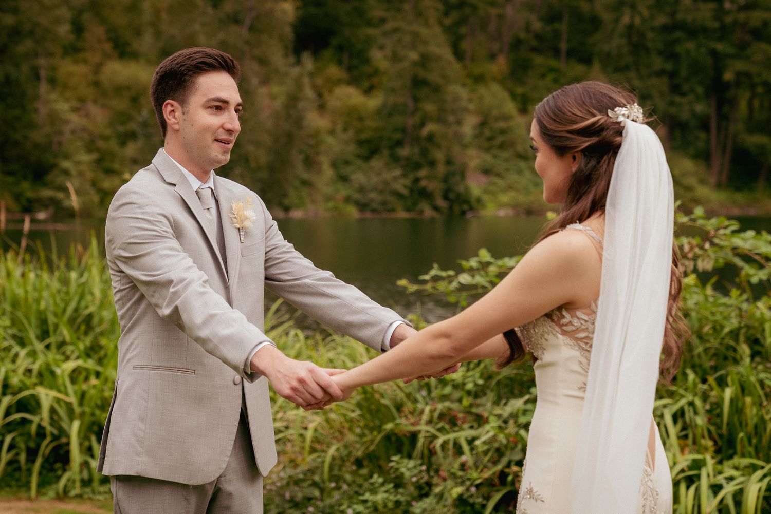 Groom and bride hold hands by lake, heartfelt outdoor Oregon vows.