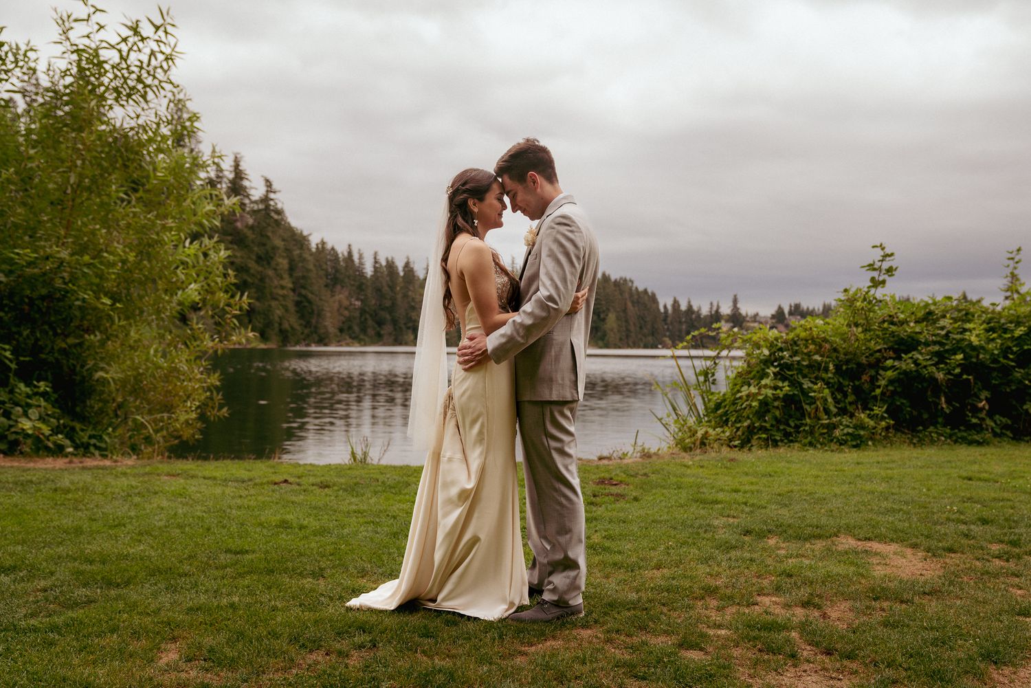 Couple kisses by lake with forest view, intimate Oregon elopement.