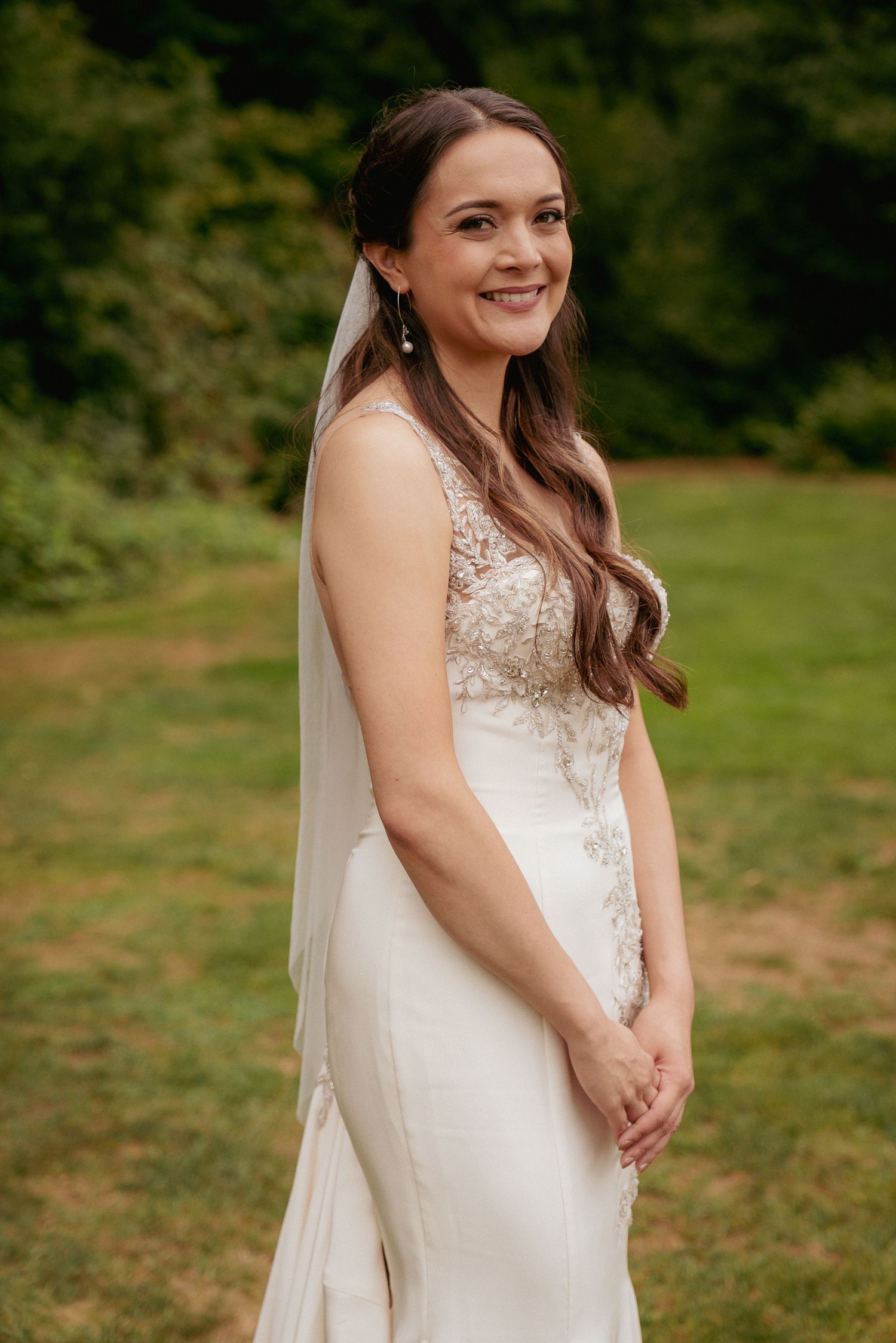 Bride smiles softly in forest light, elegant PNW wedding portrait.
