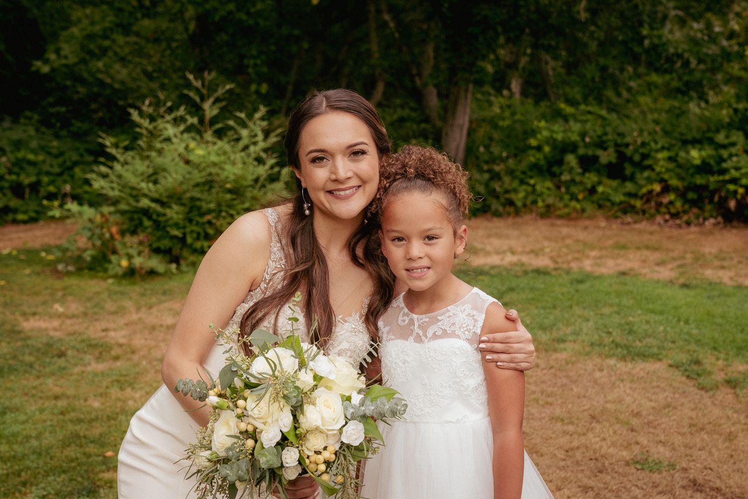 Bride with flower girl smiles, candid Oregon summer wedding portrait.