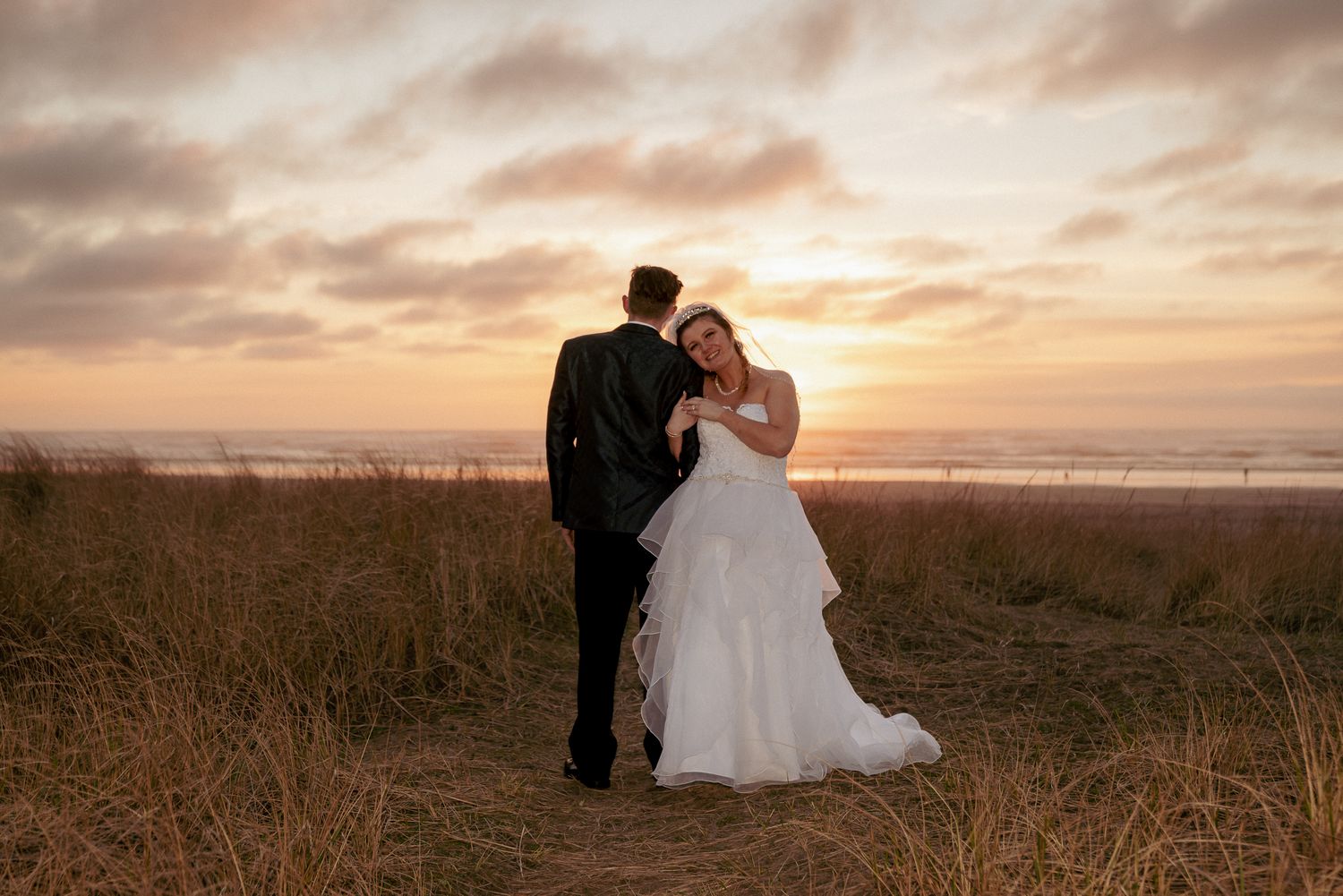 Bride and groom kiss at sunset in open Oregon field, romantic moment.