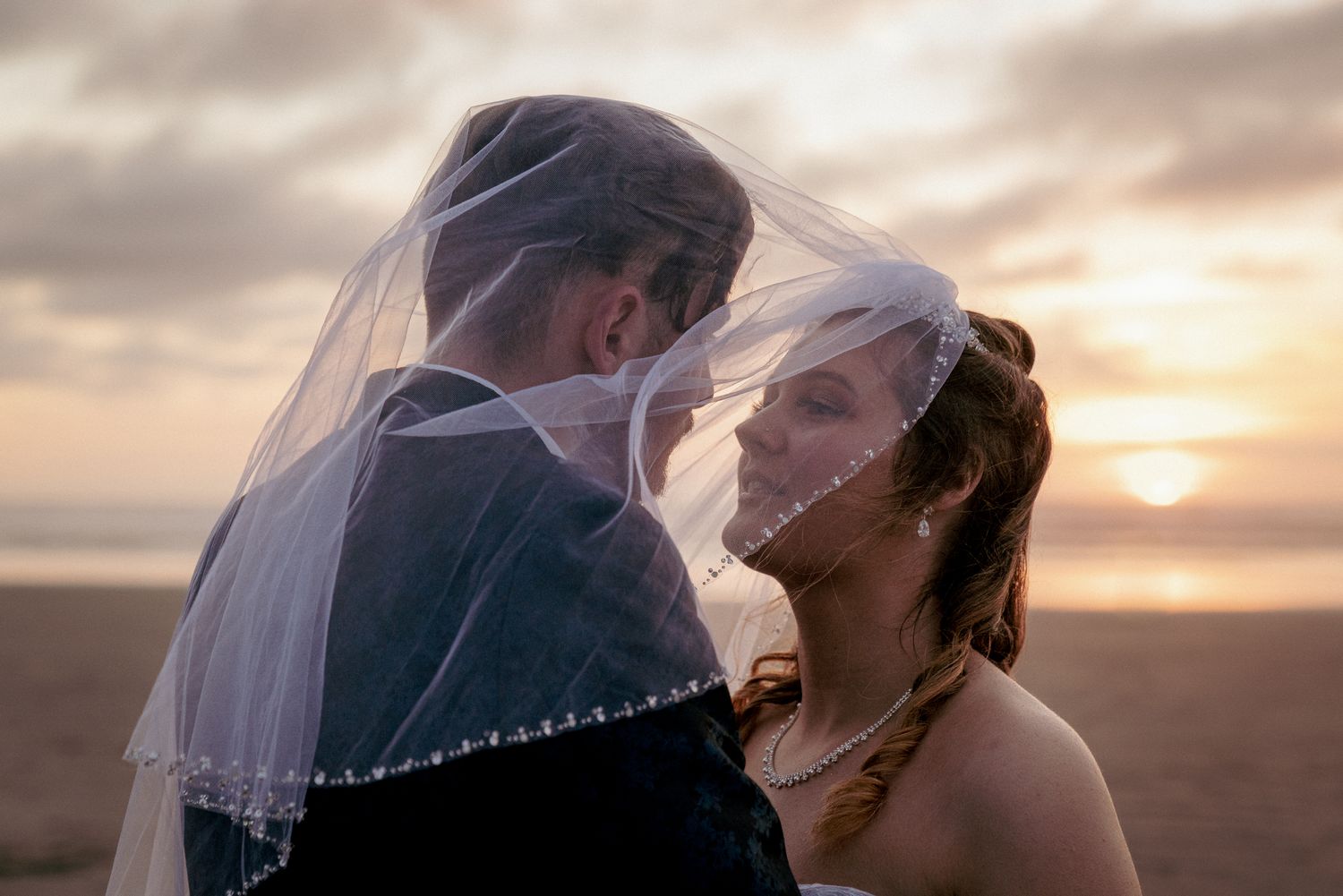 Veil-covered kiss at sunset, dreamy Oregon Coast wedding vibes.