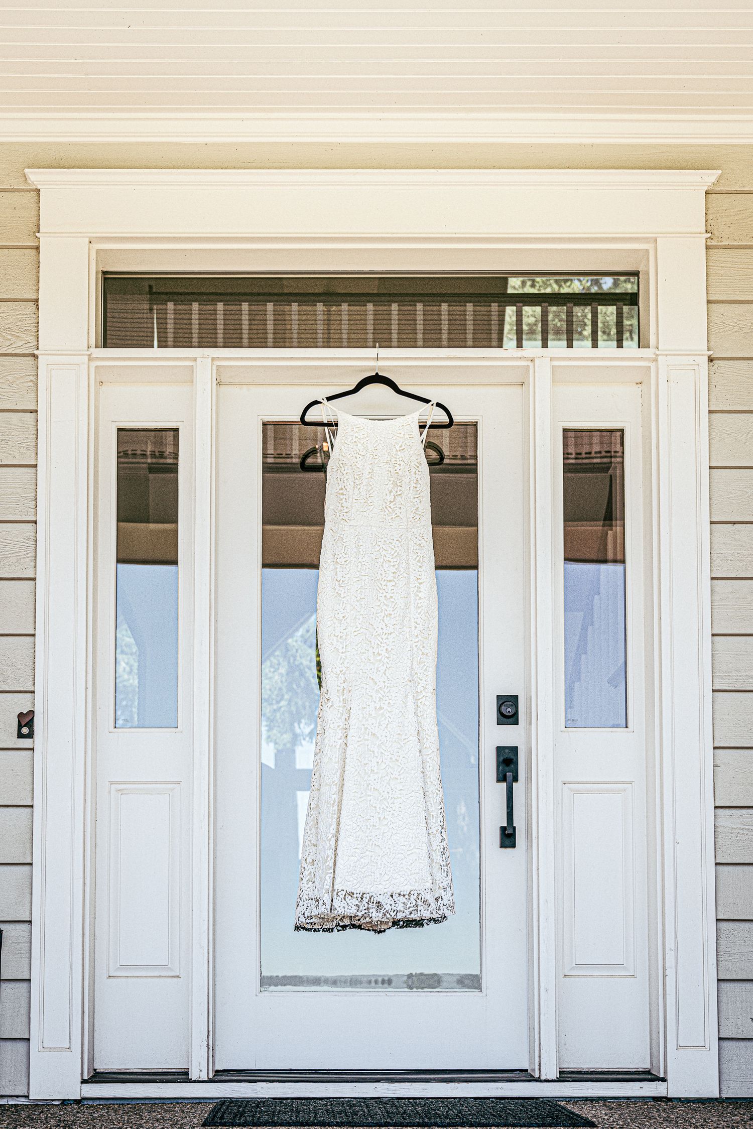 Wedding dress hangs on white door, elegant Oregon bridal prep shot.