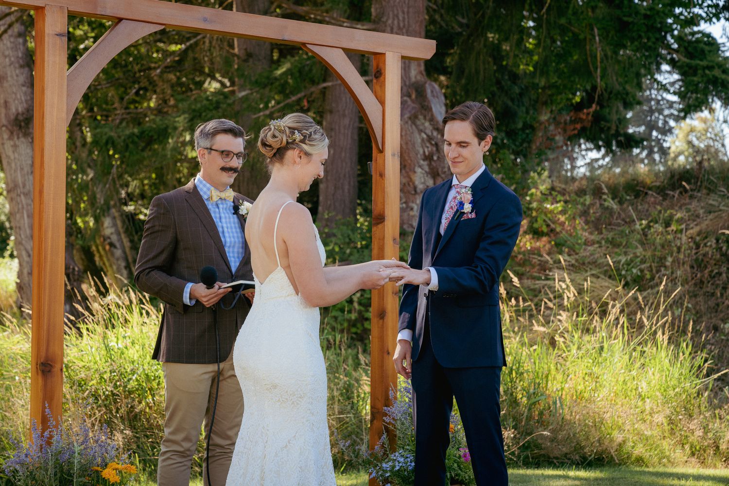 Bride says vows under wood arbor, sunny Oregon garden ceremony.
