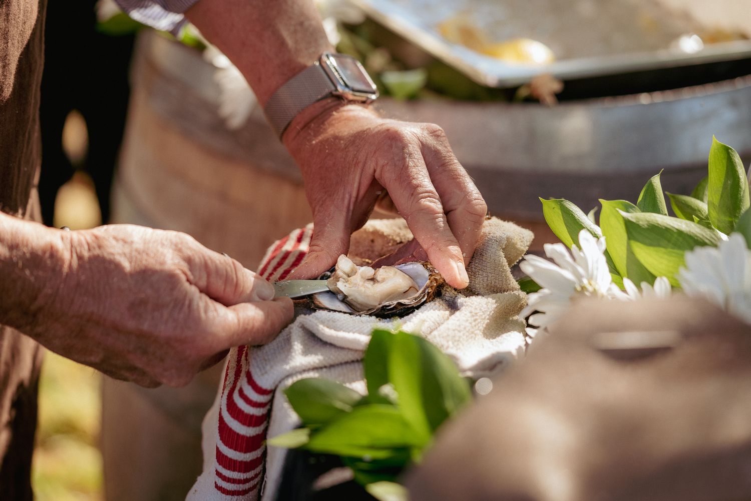 Hand holding open oyster while another hand cuts beneath the shell. Fresh oyster service at a wedding.
