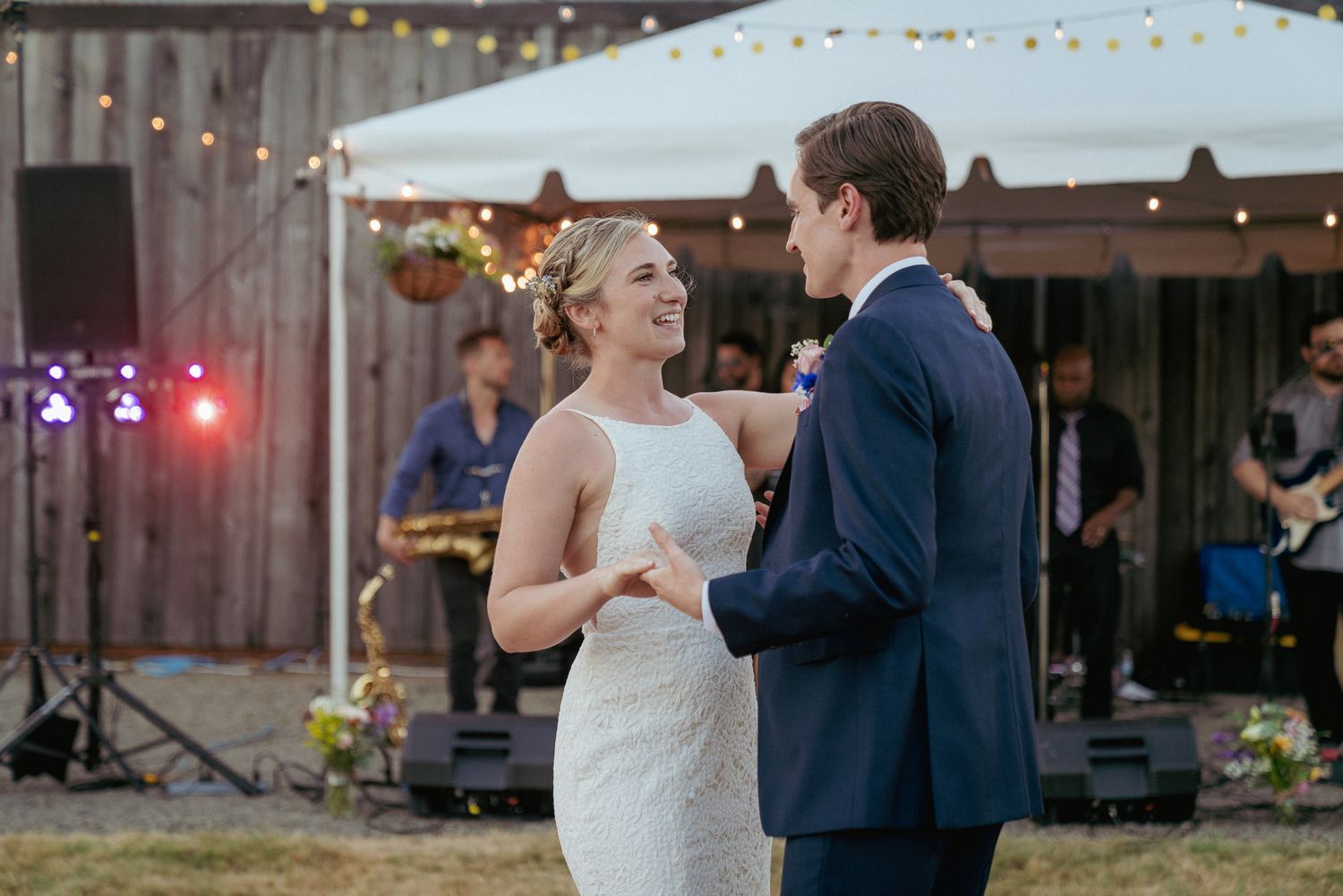Bride and groom dance under string lights, rustic barn reception with a live band.