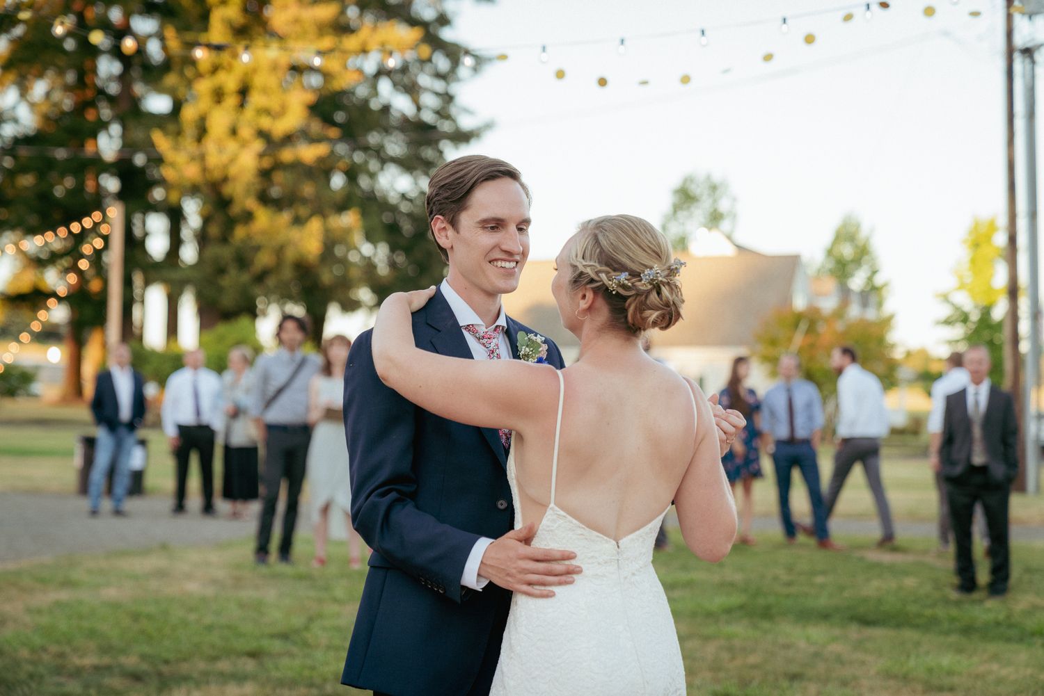 Groom and bride dance under bistro lights, PNW summer celebration.