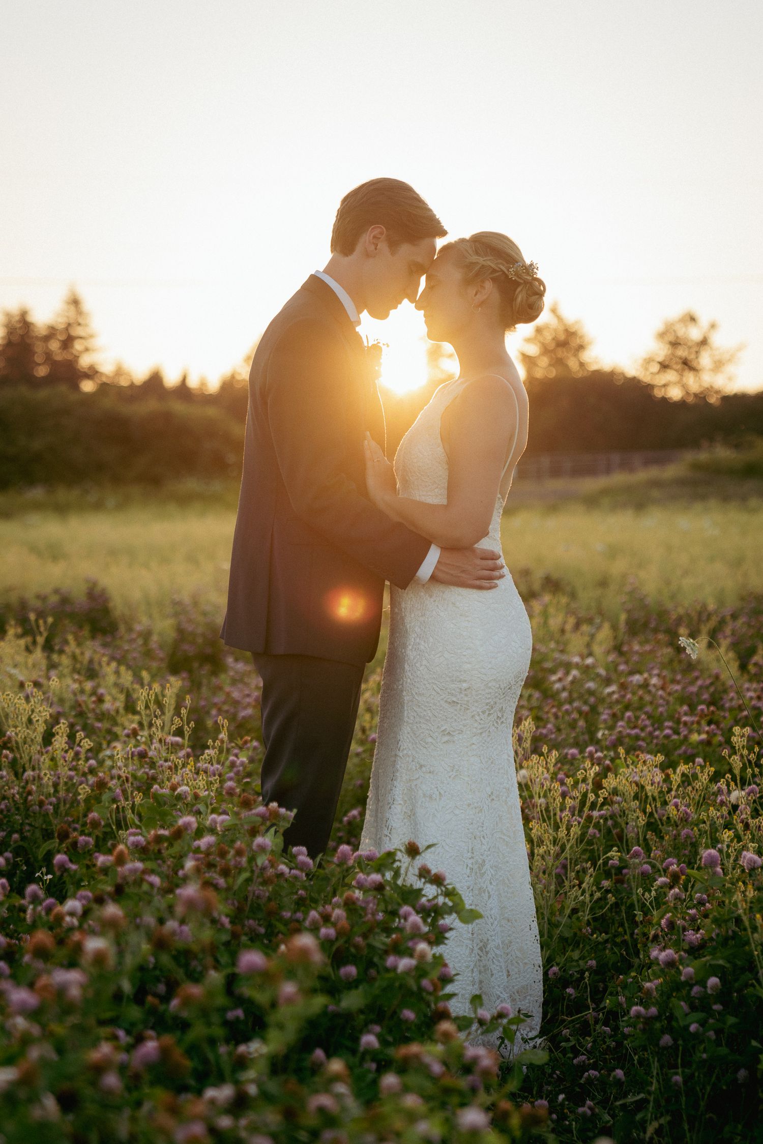 Bride and groom touch foreheads in wildflower field at sunset on private Oregon property. Golden light creates a romantic moment.