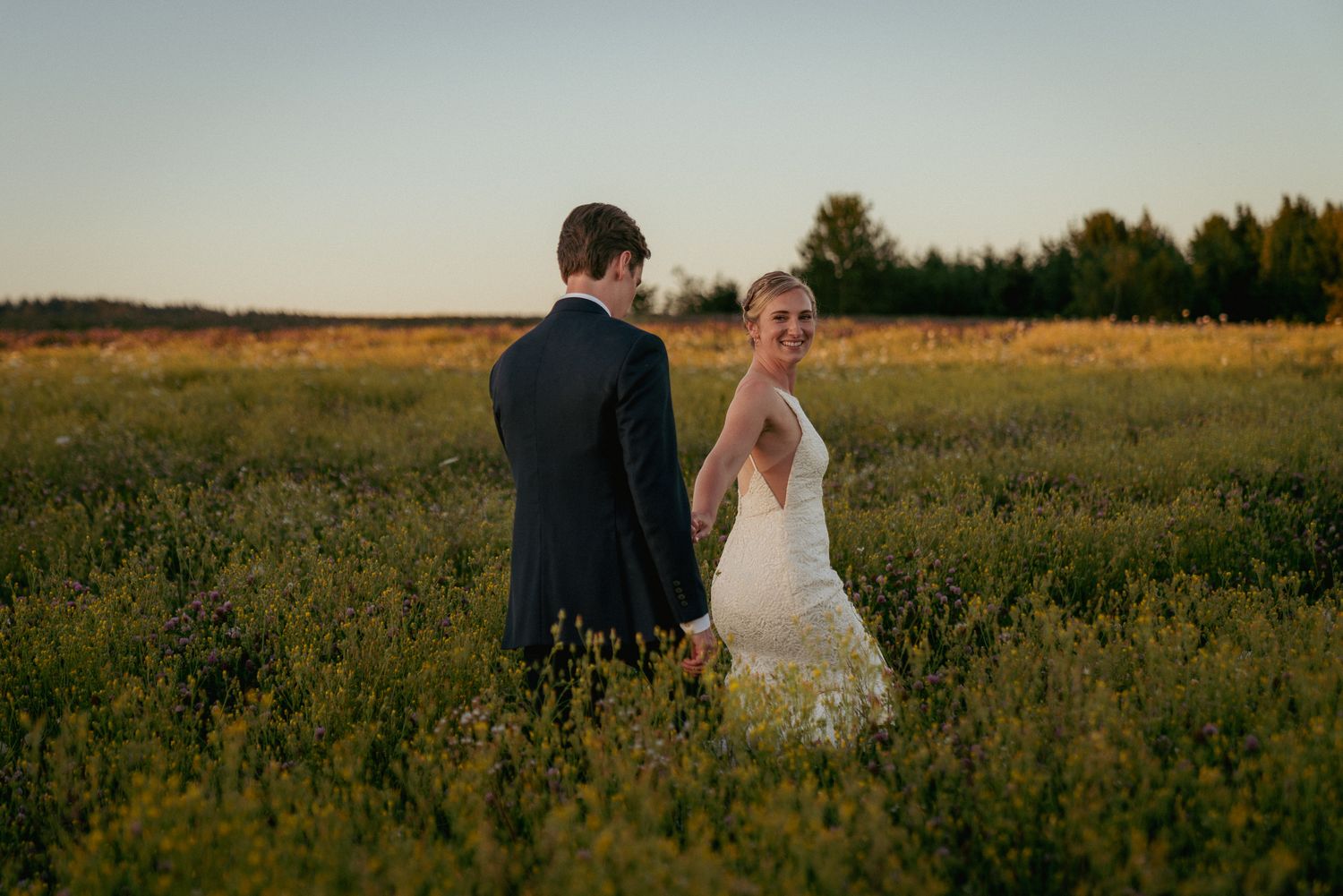 Couple walks through wildflowers at sunset, dreamy Oregon field wedding.