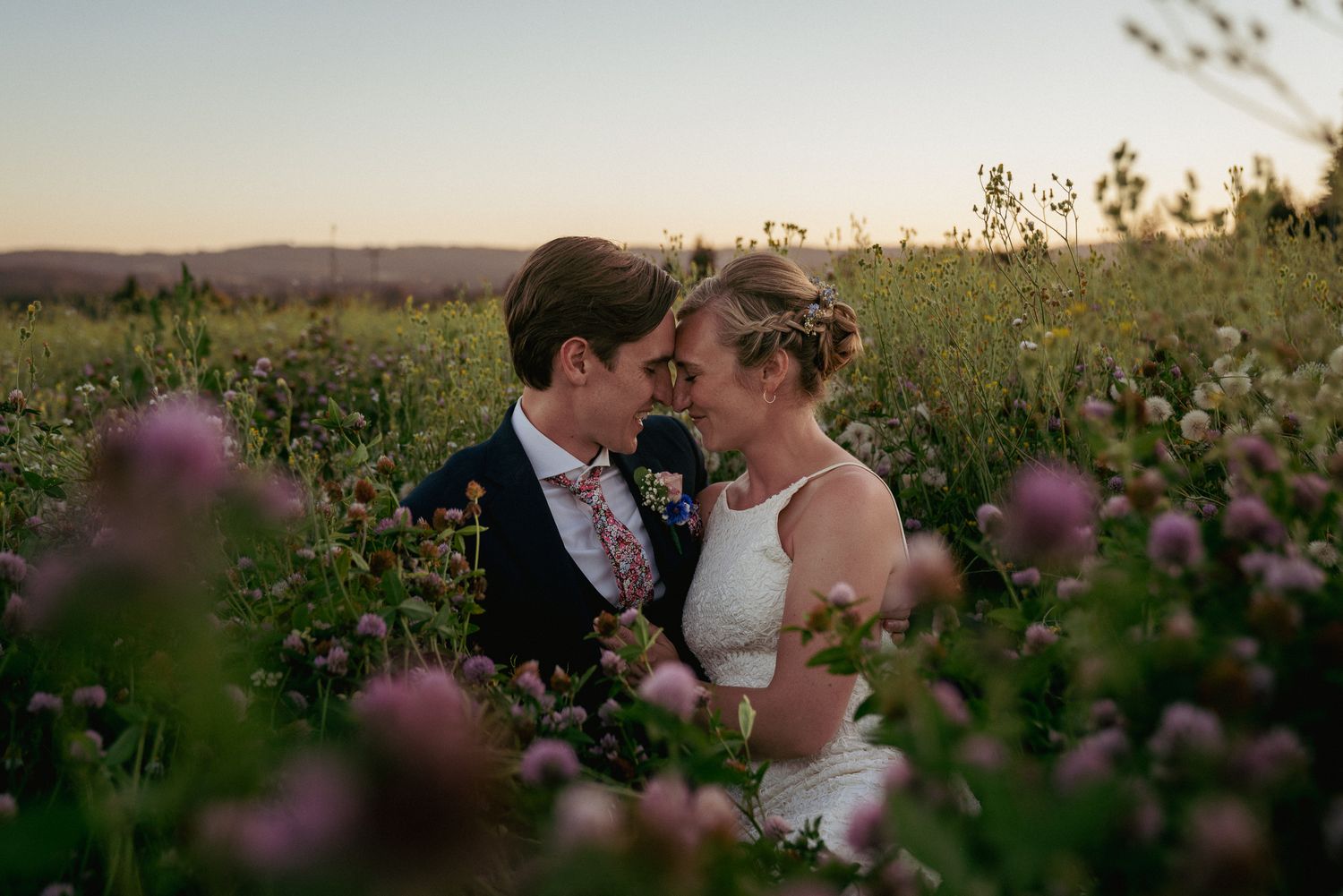 Bride and groom in a wildflower field, about to kiss. Dreamy romantic outdoor portrait.