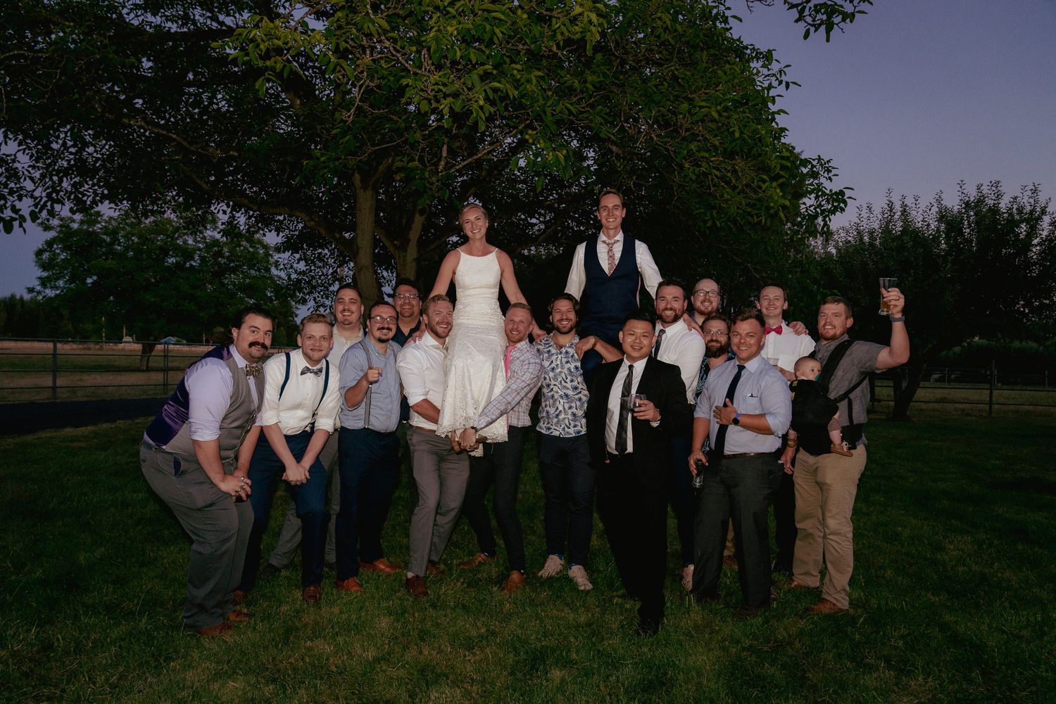 Fun wedding party lifting bride and groom outdoors, Portland summer celebration.