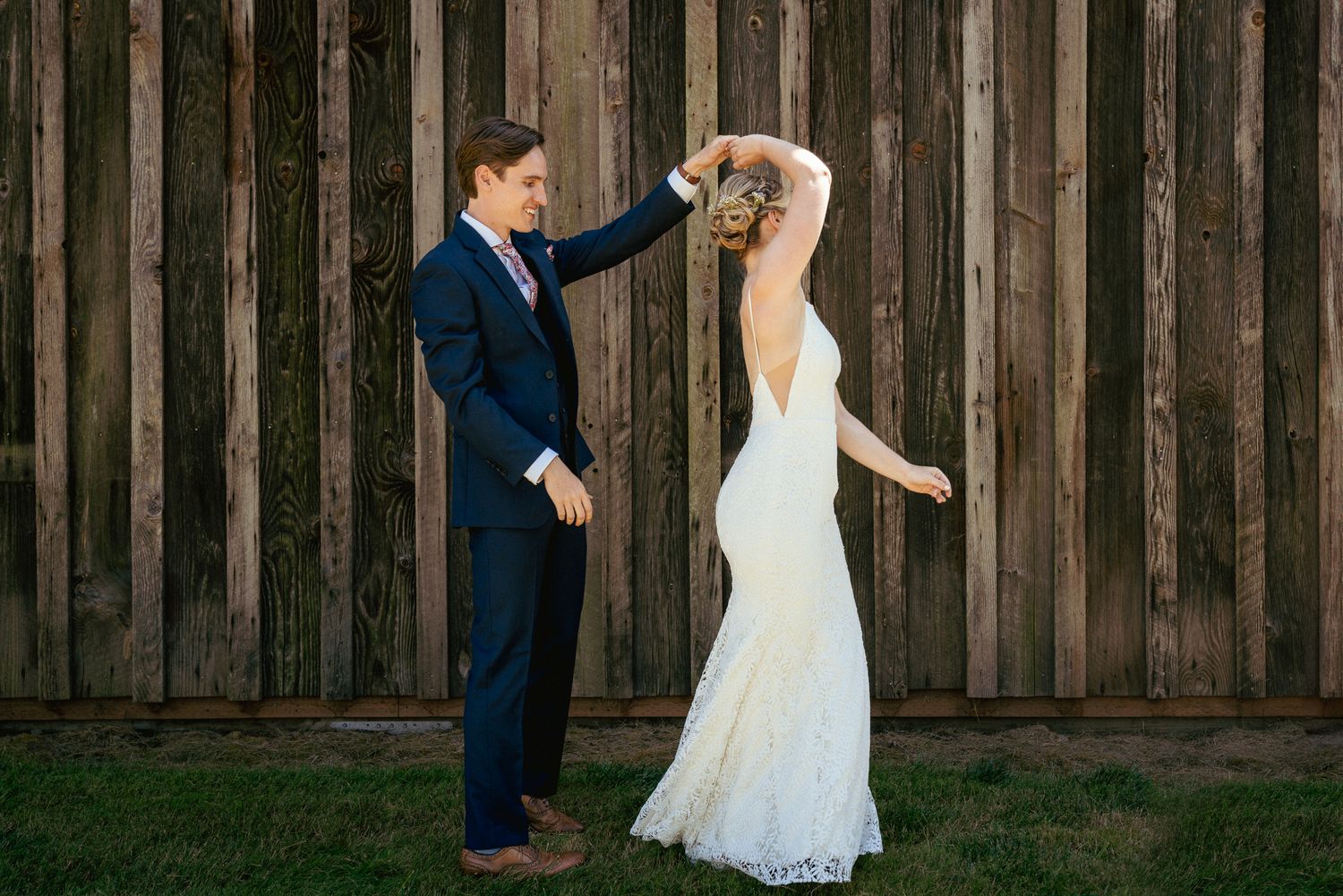Groom spins bride in front of wooden wall, rustic Oregon venue.