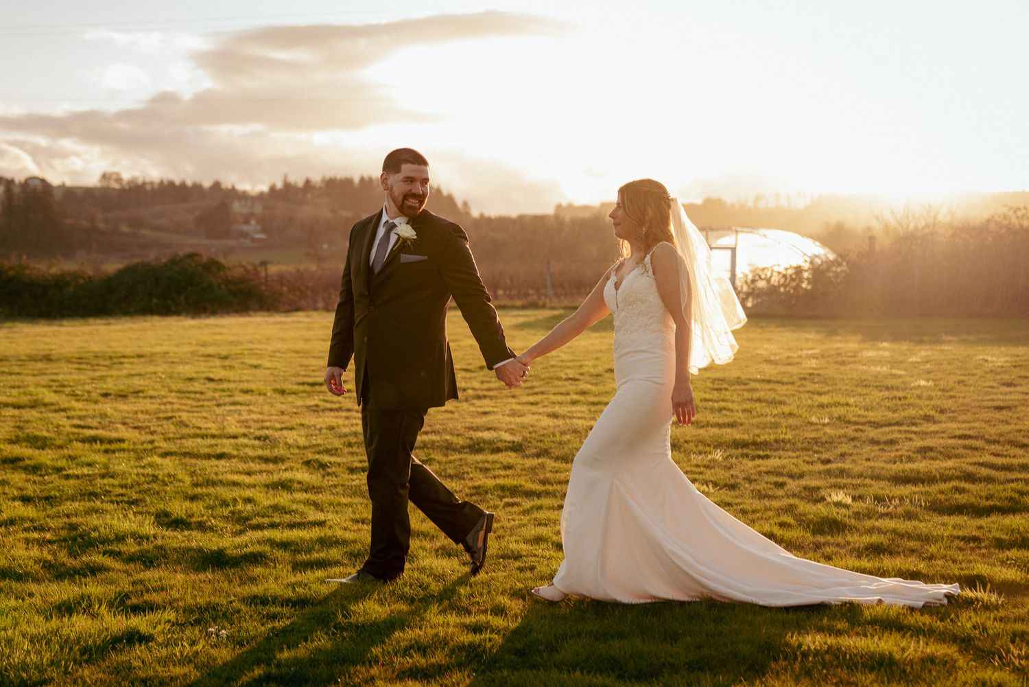 Newlyweds walk hand in hand through open field, romantic sunset wedding in the PNW.