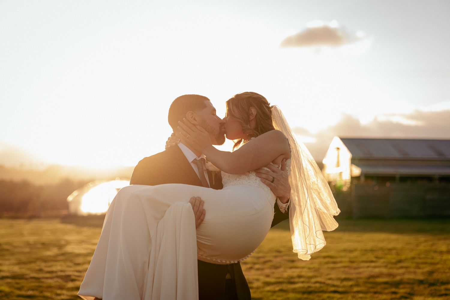 Groom lifts bride during golden hour, joyful outdoor wedding vibes.