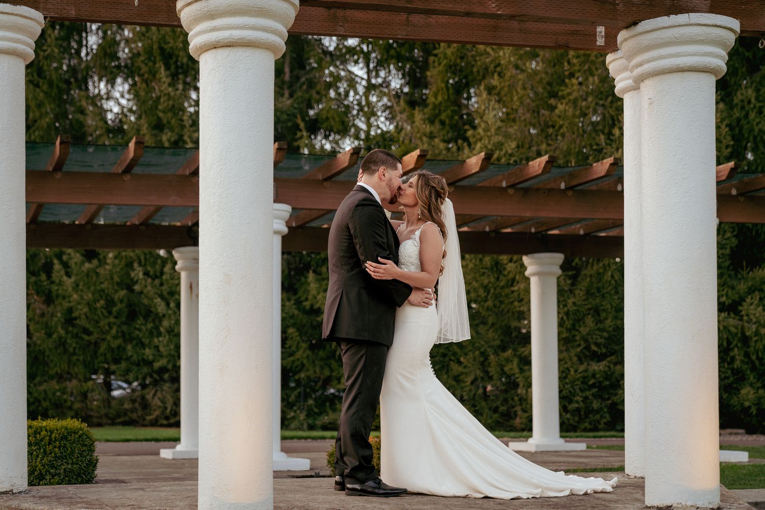 Romantic kiss under white columns, classic PNW garden wedding.
