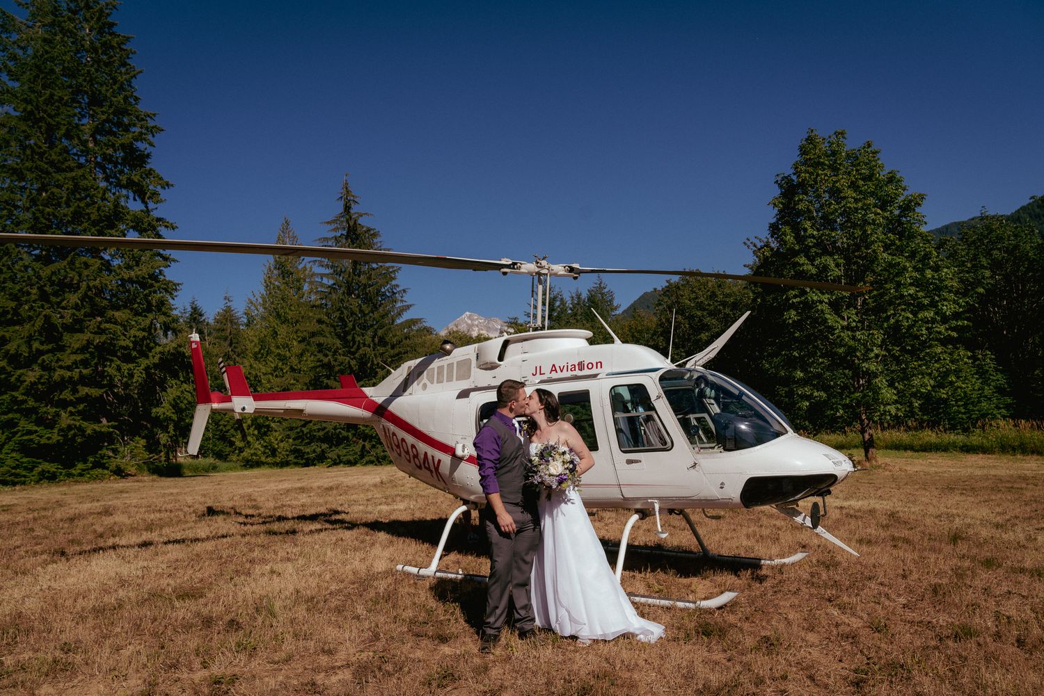 Couple kisses in front of helicopter, adventurous Oregon wedding around Mt. Hood.