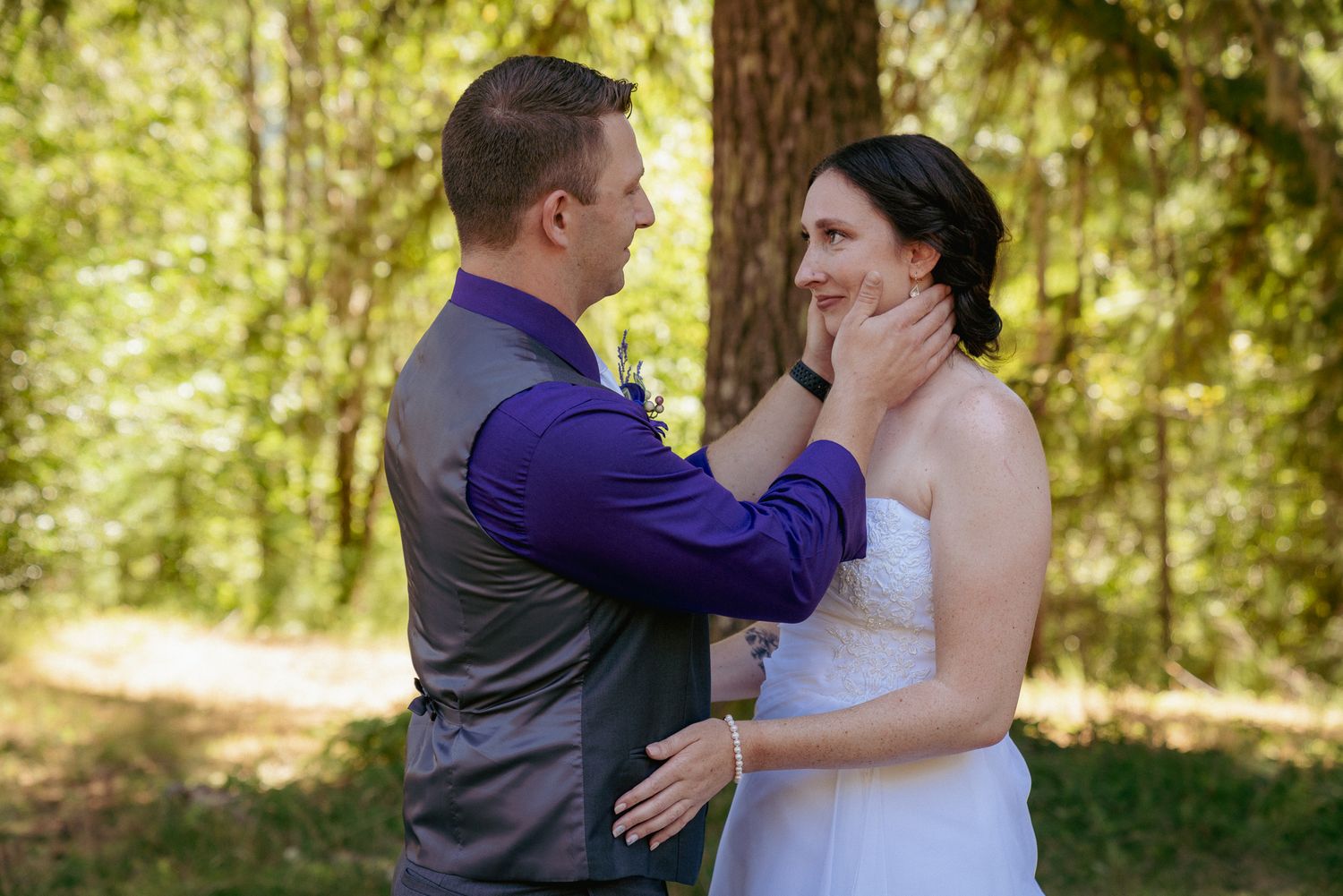 Groom touches bride’s cheek, sweet moment in PNW pine forest.