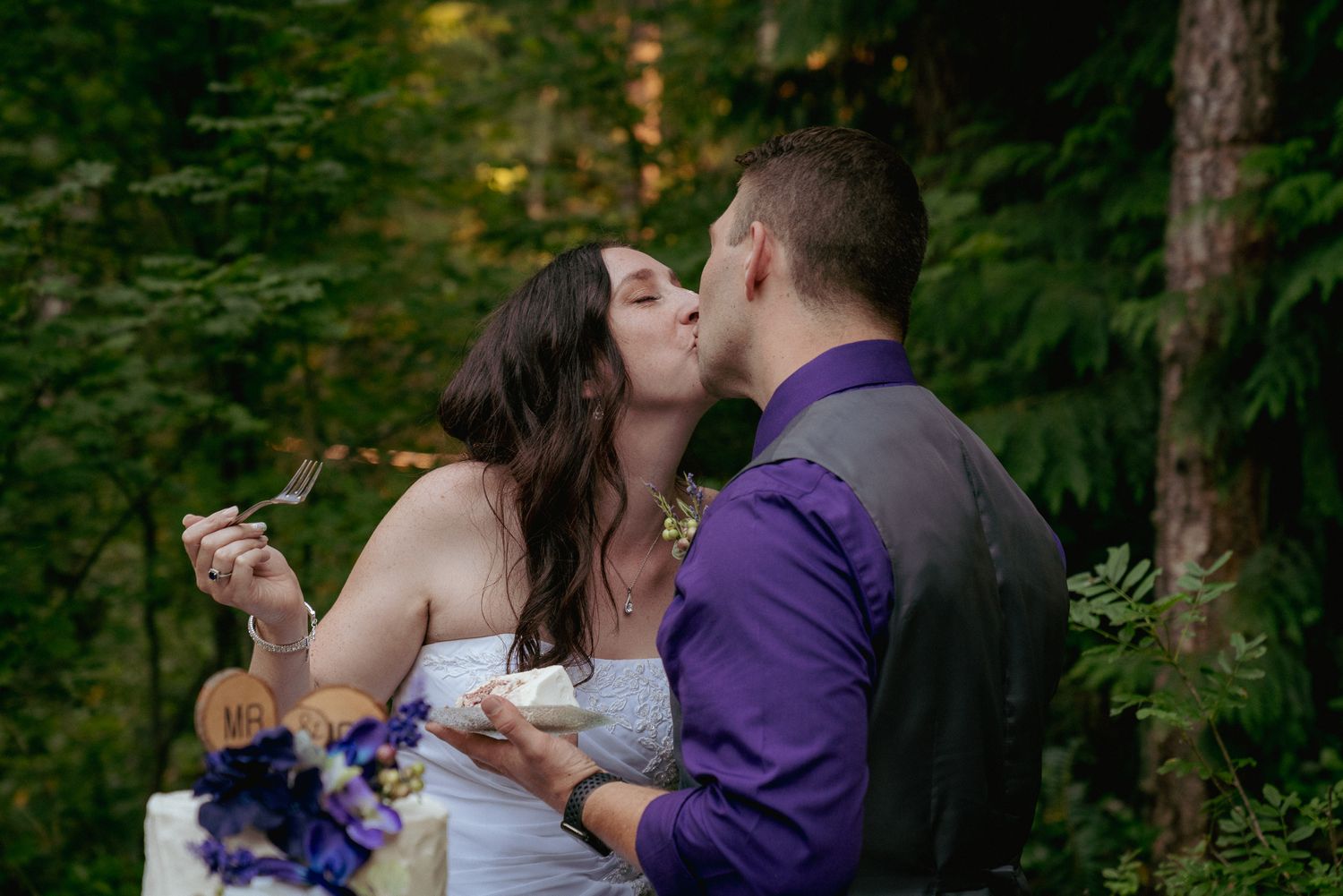 Bride and groom sharing a sweet kiss after cake cutting, holding purple bouquet, PNW elopement.